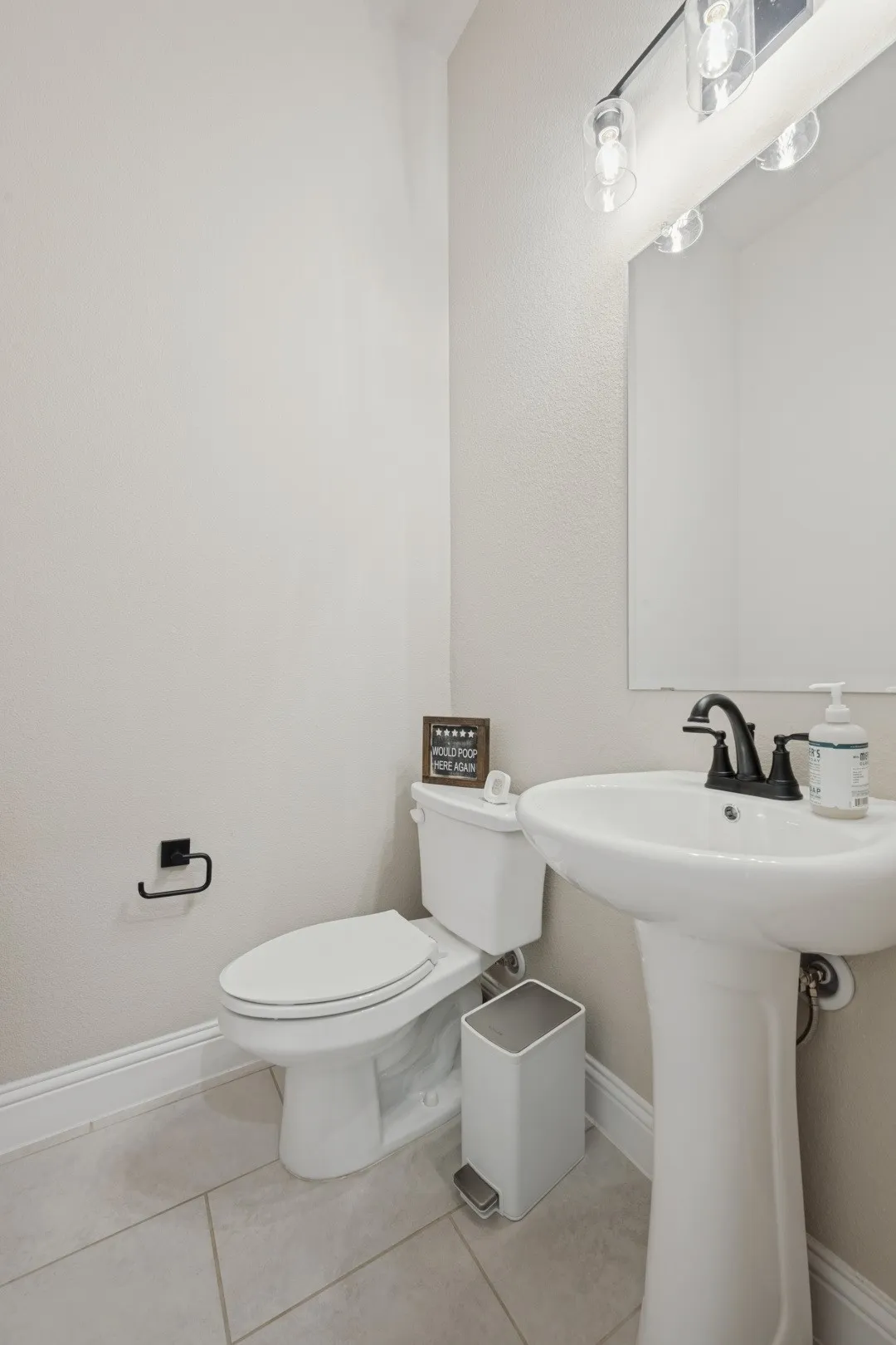 Pedestal sink with a matte black faucet, ceramic tile flooring, and a wall-mounted vanity light