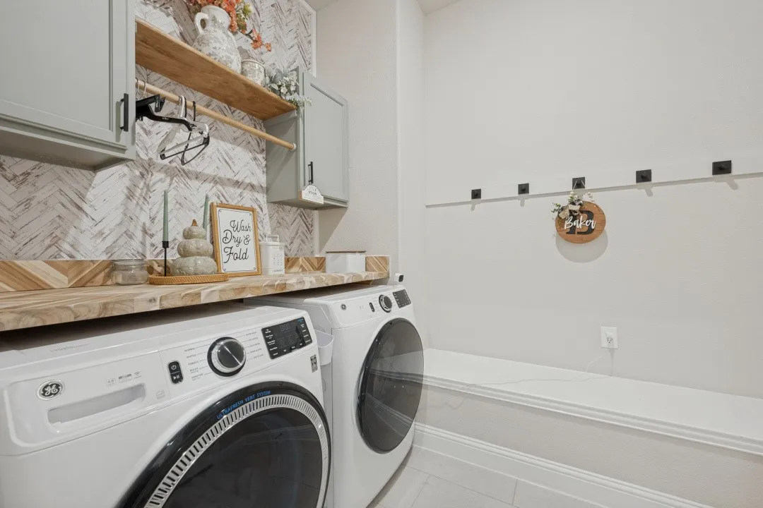 Wood-finish countertop with herringbone pattern backsplash, light gray cabinetry, and a built-in hanging rod
