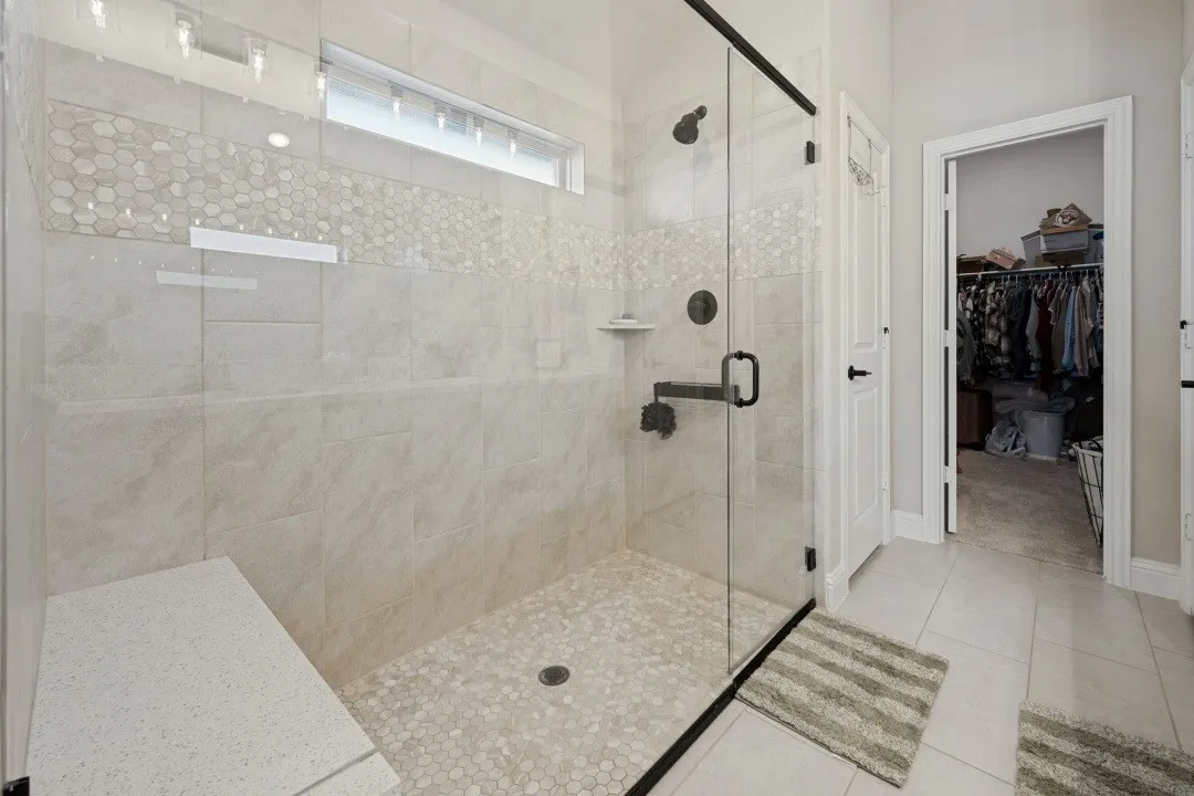 Glass-enclosed shower with matte black fixtures, integrated bench, pebble-tile flooring, and a transom window