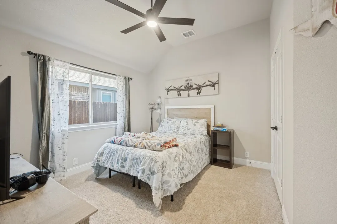 Bright secondary bedroom with ceiling fan, large window with natural light, neutral carpet flooring, and metal bed frame