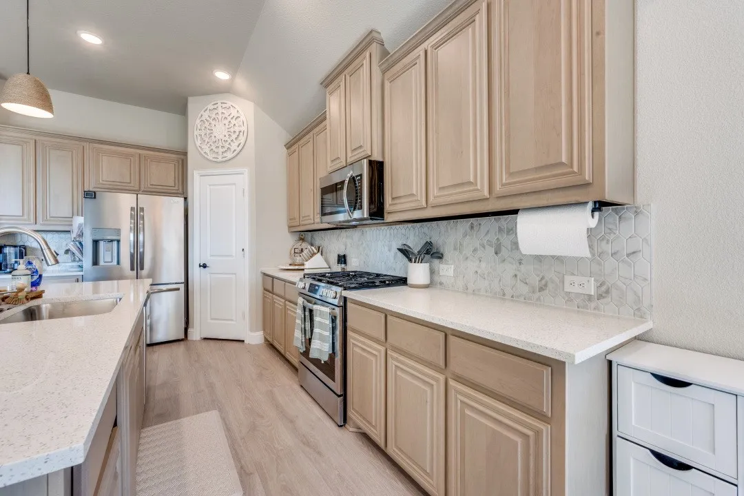 Kitchen featuring wood-finish cabinetry, stainless steel appliances, light-colored countertops, a geometric tile backsplash, and wood-finish flooring