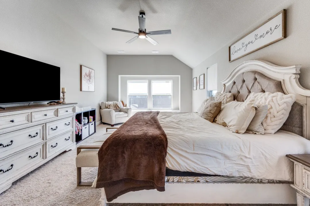 Primary bedroom suite featuring a decorative upholstered headboard with nailhead trim, ceiling fan with integrated lighting, white cabinetry with hardware accents, and direct access to natural light through dual windows