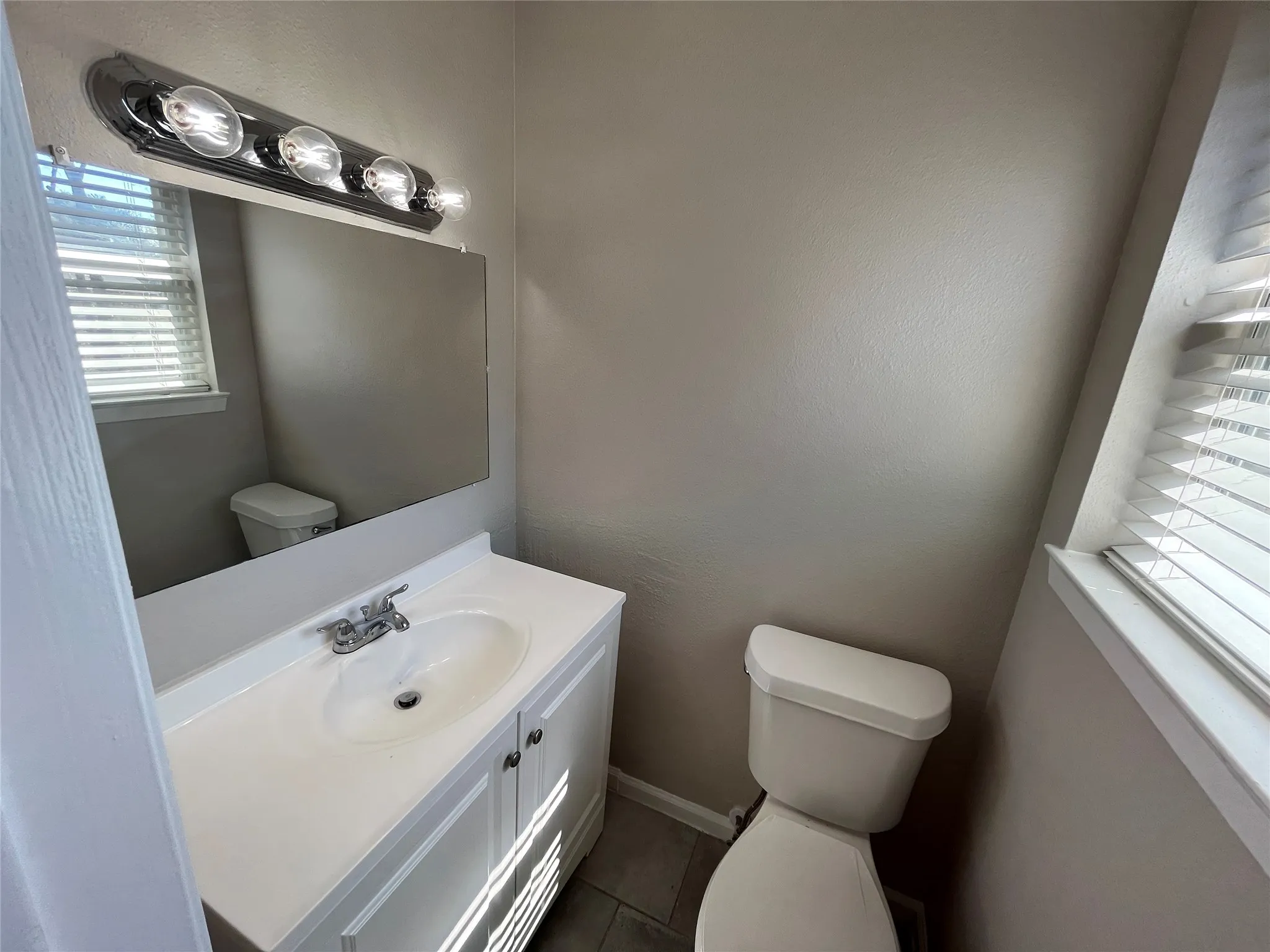 White vanity with integrated sink, rectangular mirror, and chrome vanity light fixture