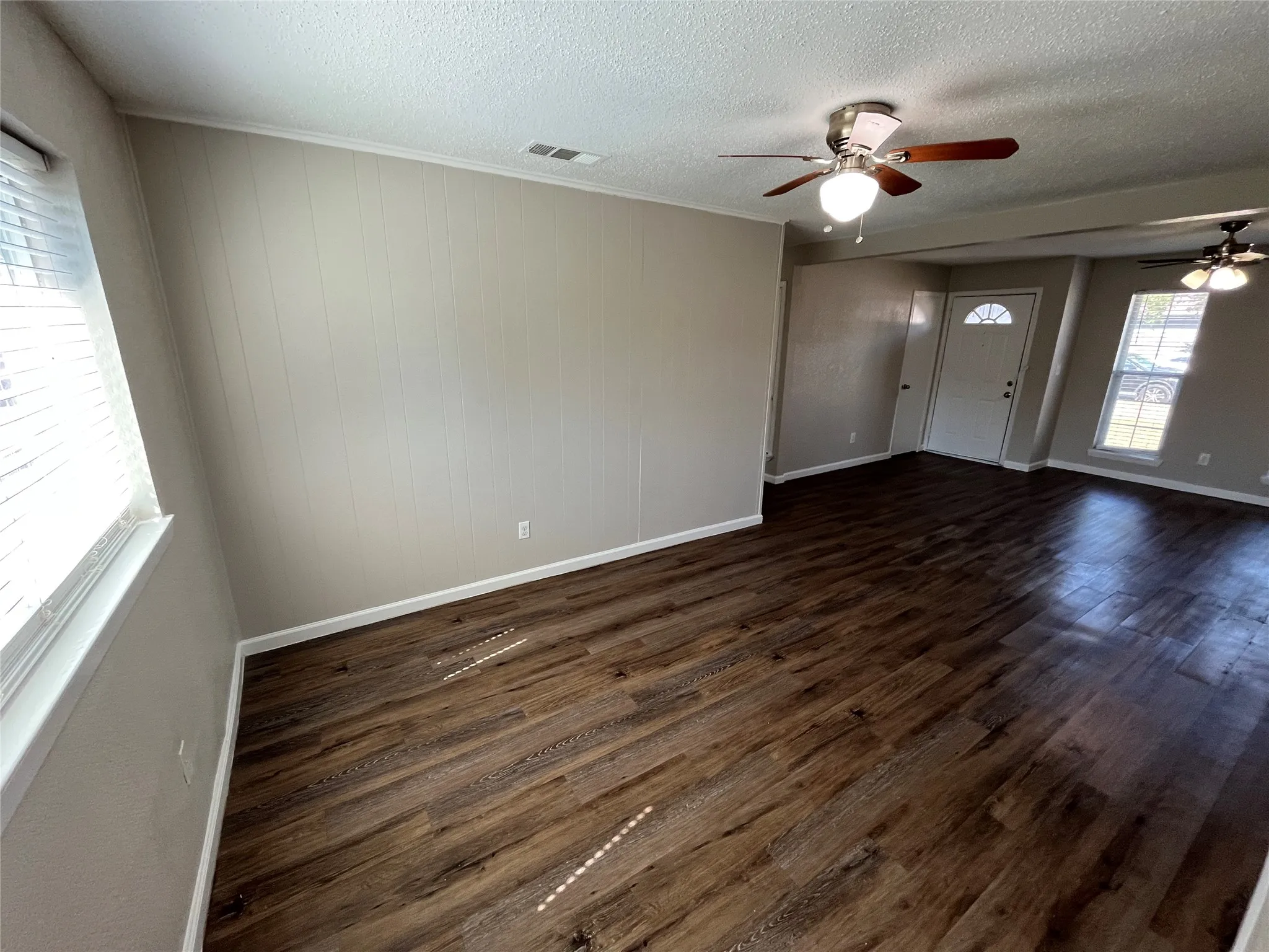 Wood-finish flooring, white trim, paneled wall accent, and ceiling fans with integrated lighting