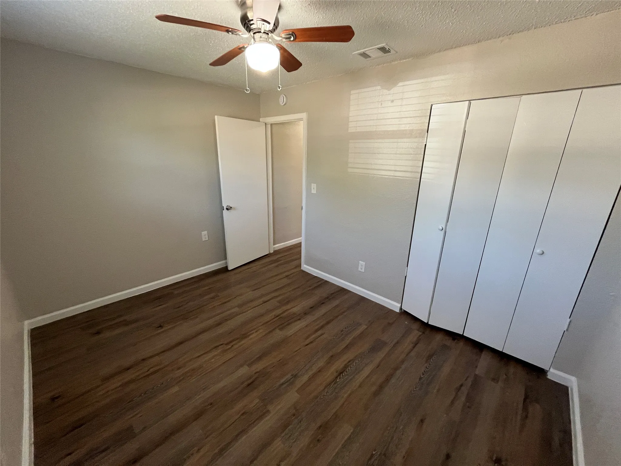 Wood-finish flooring, ceiling fan with integrated lighting, bi-fold closet doors, and neutral wall paint