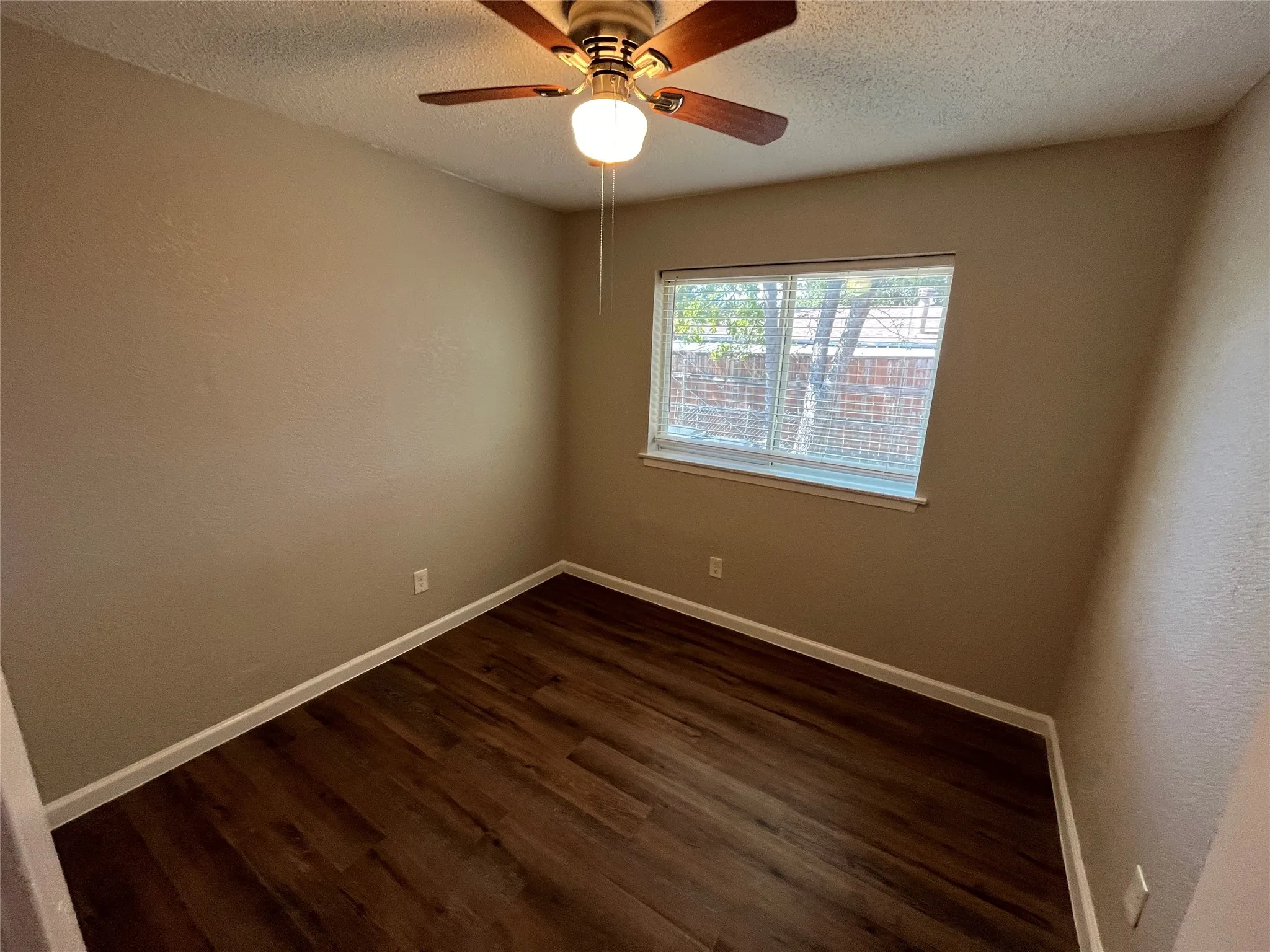 Wood-finish flooring, neutral wall tones, ceiling fan with integrated lighting, and a large window with blinds