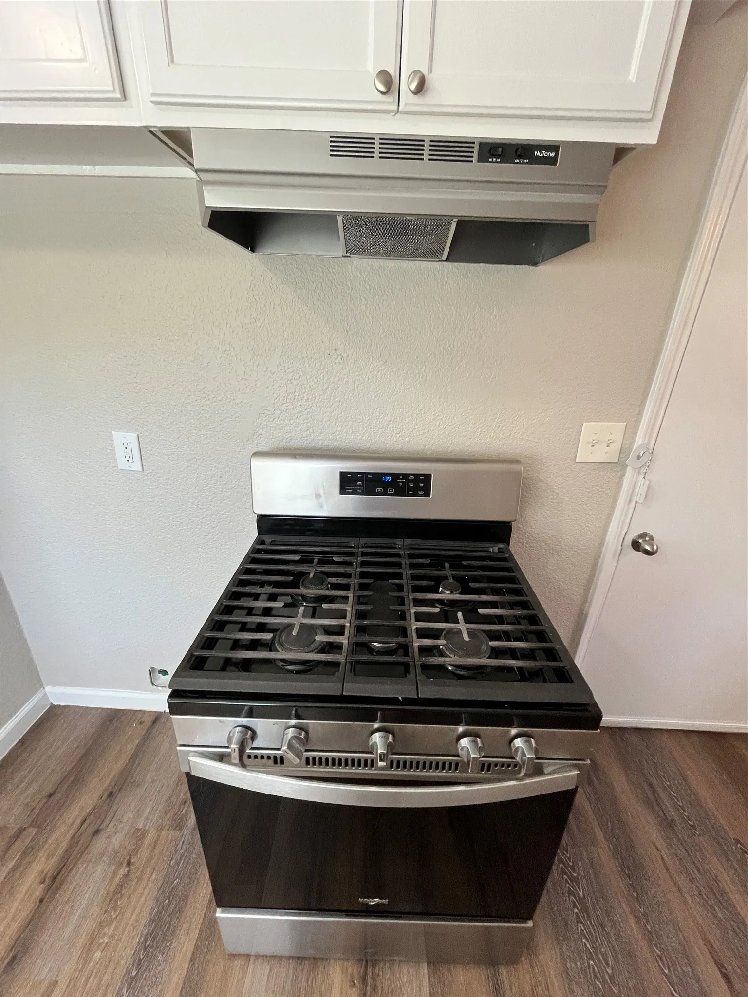 Stainless steel gas range with a black cooktop, under-cabinet range hood, white upper cabinetry, and wood-finish flooring