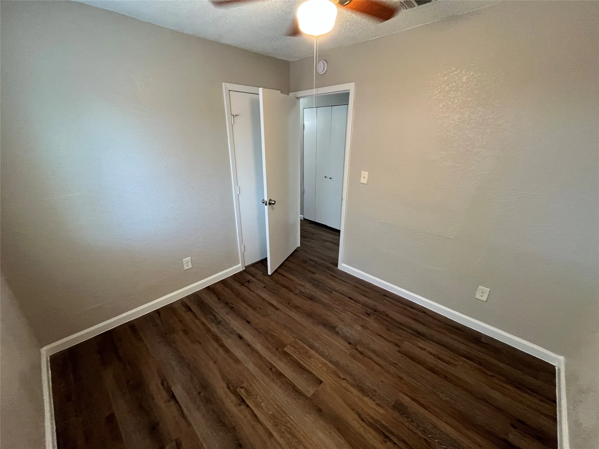 Wood-finish flooring, neutral wall tones, ceiling fan with integrated lighting, and white trim
