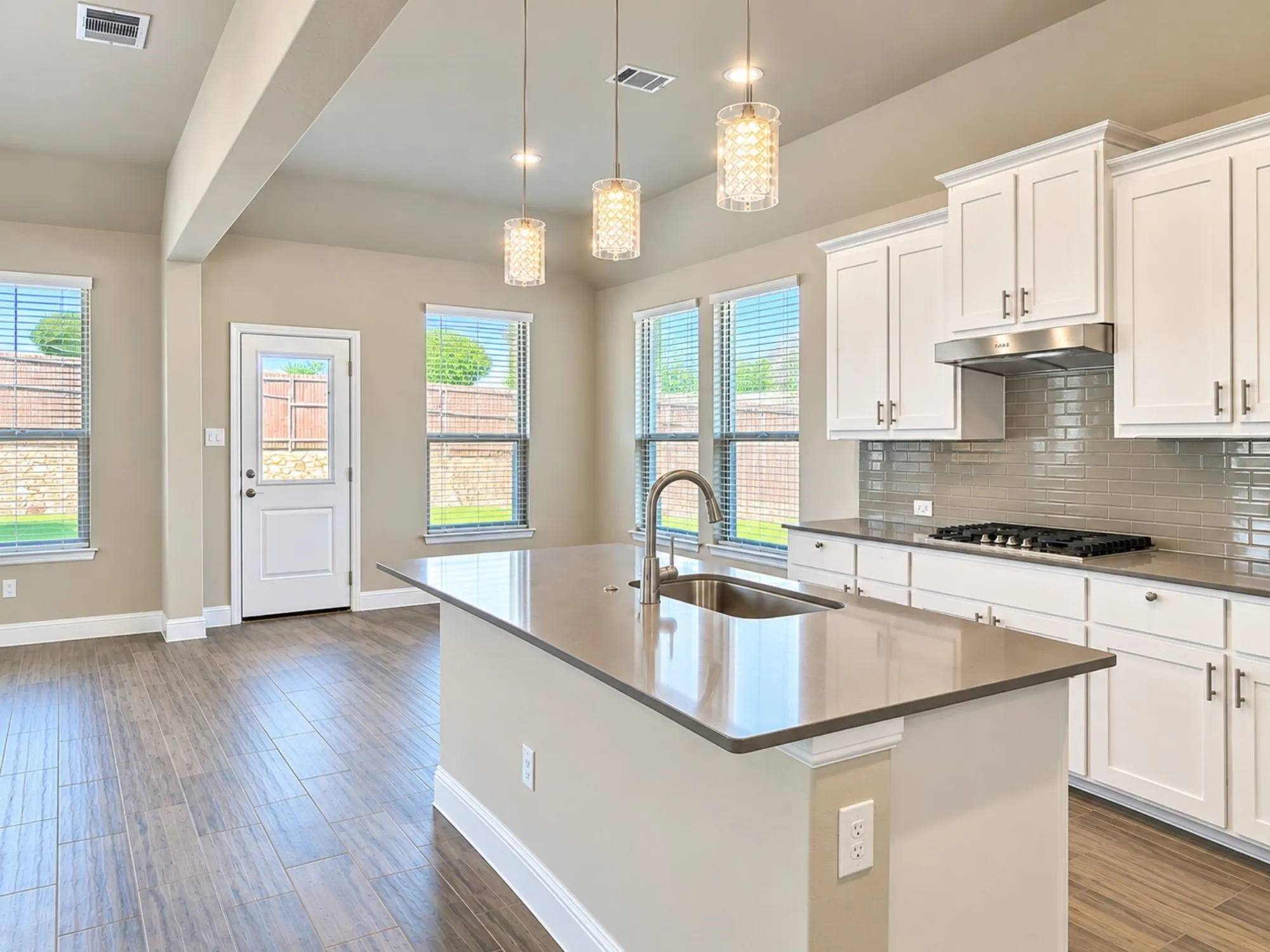 Kitchen featuring a central island with an undermount sink, white shaker-style cabinetry, stainless steel appliances, a tiled backsplash, and wood-finish flooring