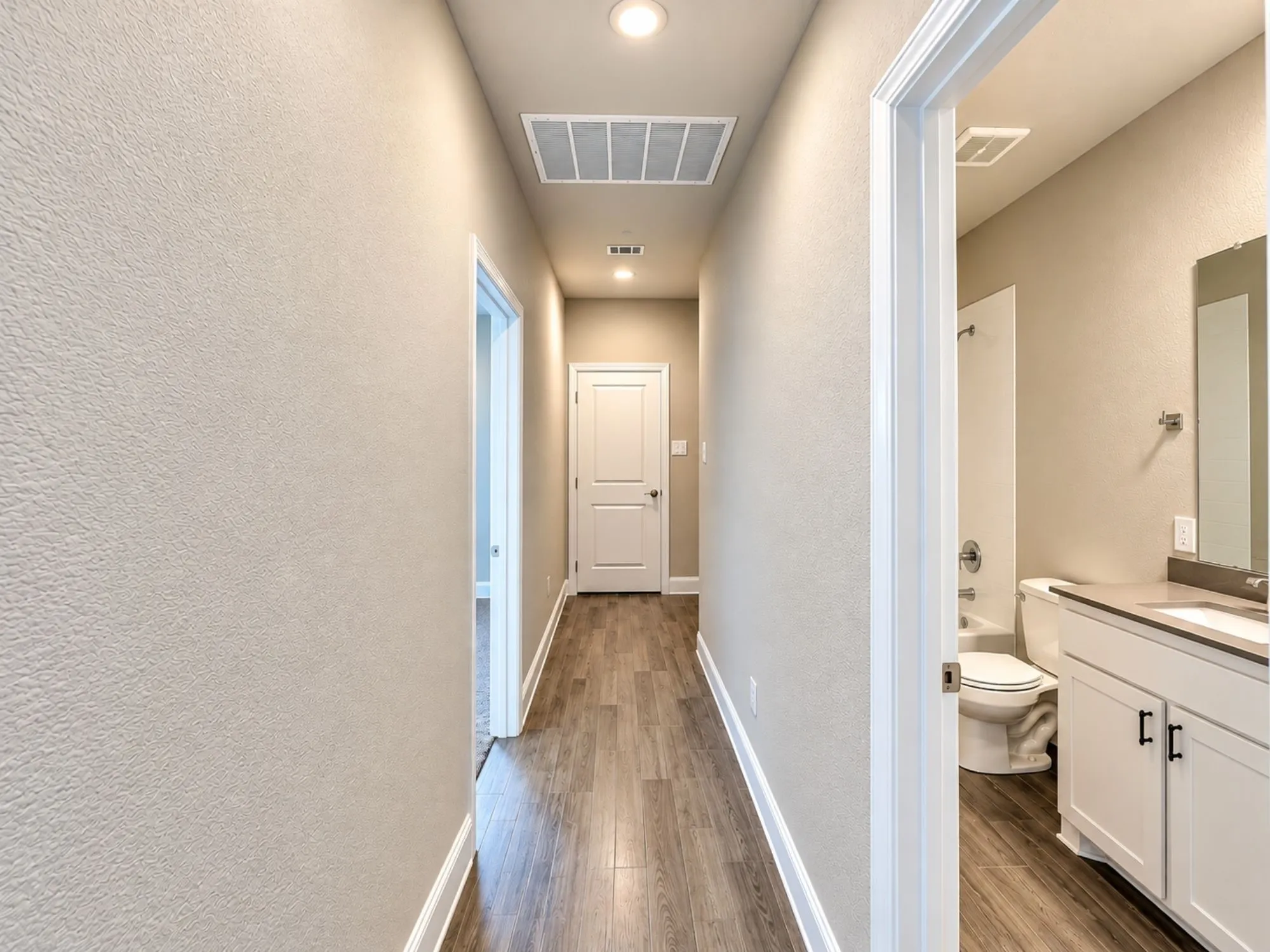 Bright hallway with recessed ceiling lighting, wood-finish flooring throughout, and fresh neutral wall finishes