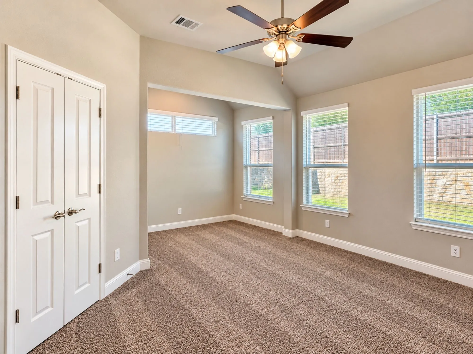 Vaulted ceiling with a ceiling fan, three large windows, textured carpeting, and double-door closet