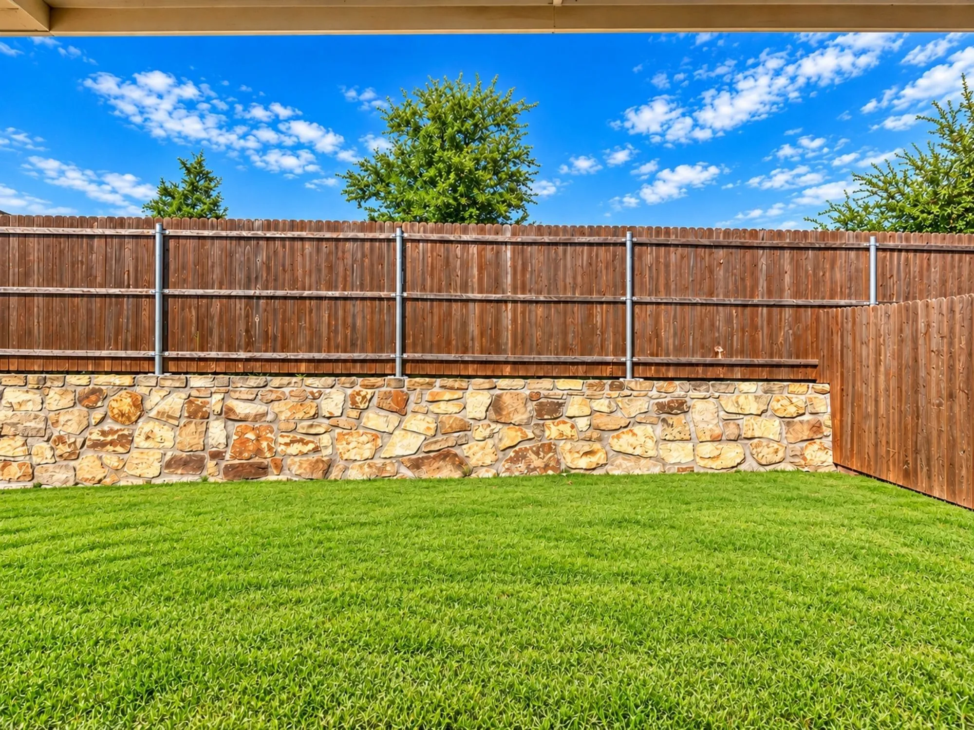 Expansive backyard showcasing a manicured lawn, stone retaining wall, and sturdy wood-finish fencing with metal frame reinforcement