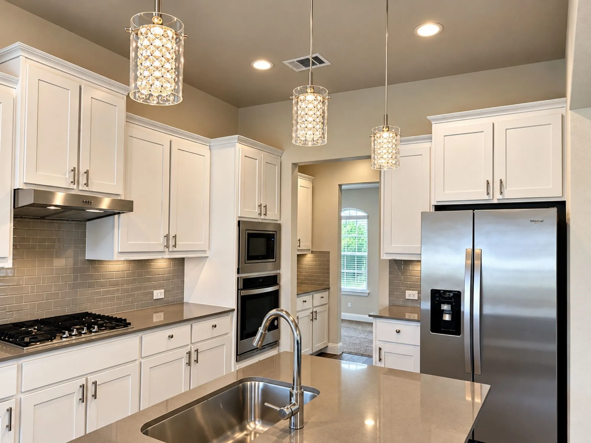 Chef's kitchen featuring white cabinetry with brushed nickel hardware, stainless steel appliances including a side-by-side refrigerator and dual wall ovens, quartz countertops, a gas cooktop with stainless steel hood, subway tile backsplash, and a large center island with undermount sink and chrome faucet