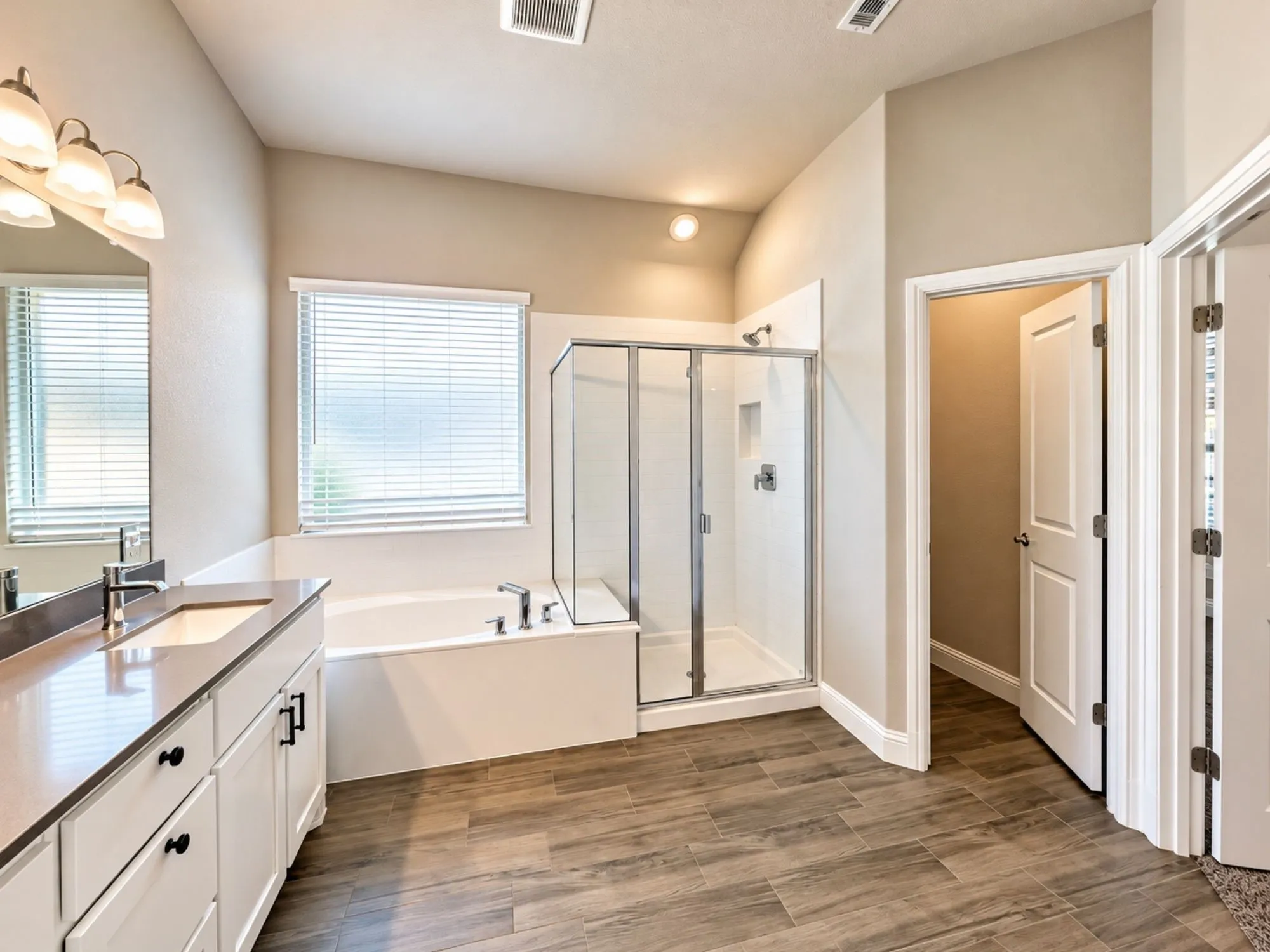 Wood-finish tile flooring, a built-in soaking tub, a separate glass-enclosed shower, a vanity with a countertop, and recessed lighting