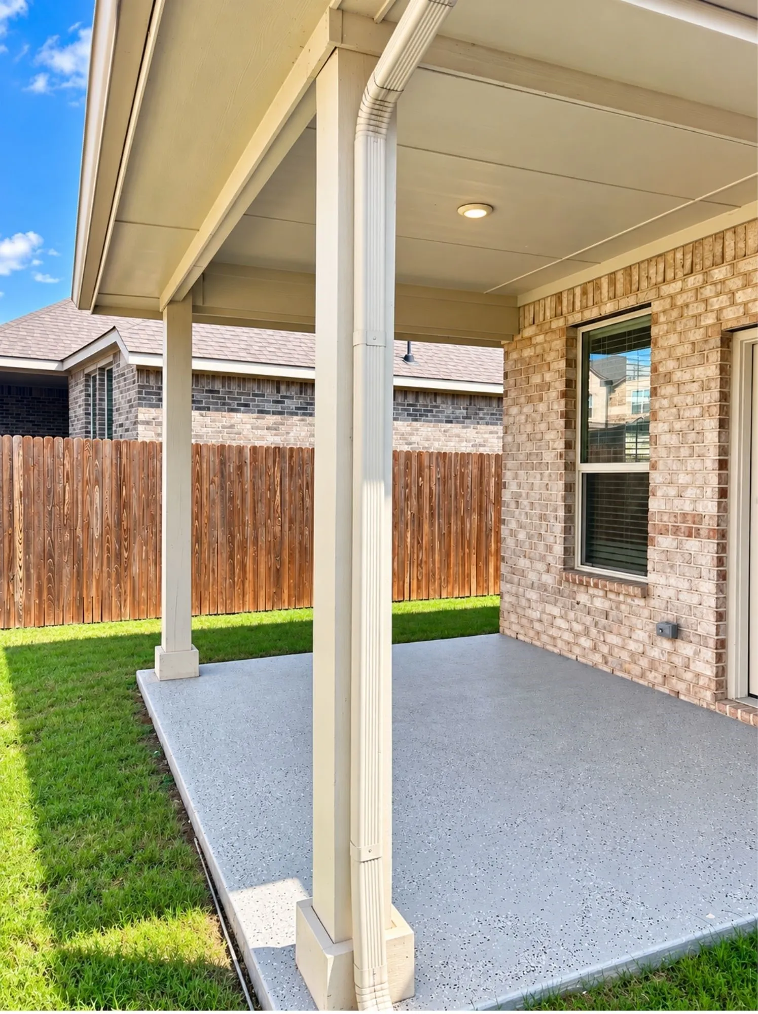 Covered patio with integrated lighting, brick exterior wall, and fenced backyard