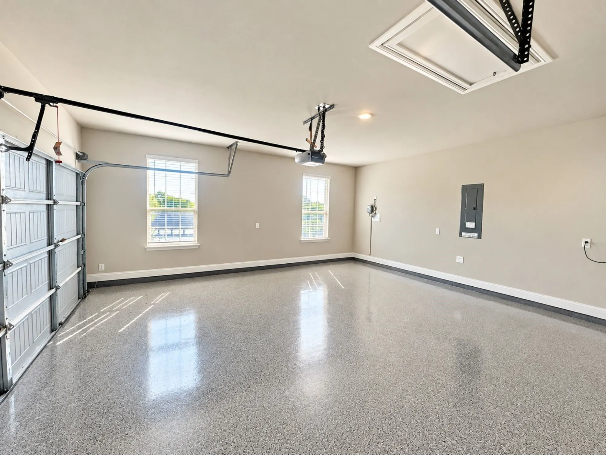 Expansive garage with a speckled epoxy floor finish, two windows, and overhead lighting
