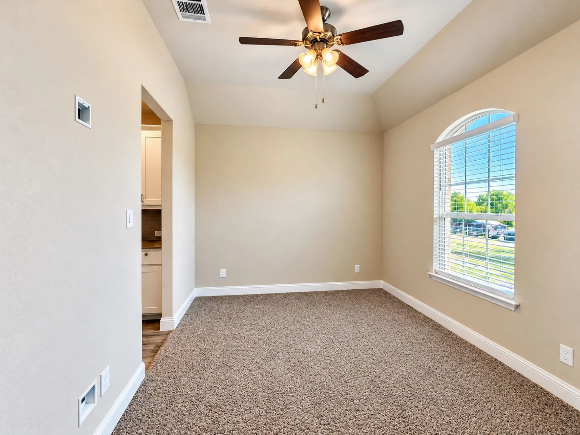 Spacious bedroom featuring neutral wall finishes, plush carpet flooring, arched window with natural light, ceiling fan with integrated lighting, and direct access to an ensuite bathroom