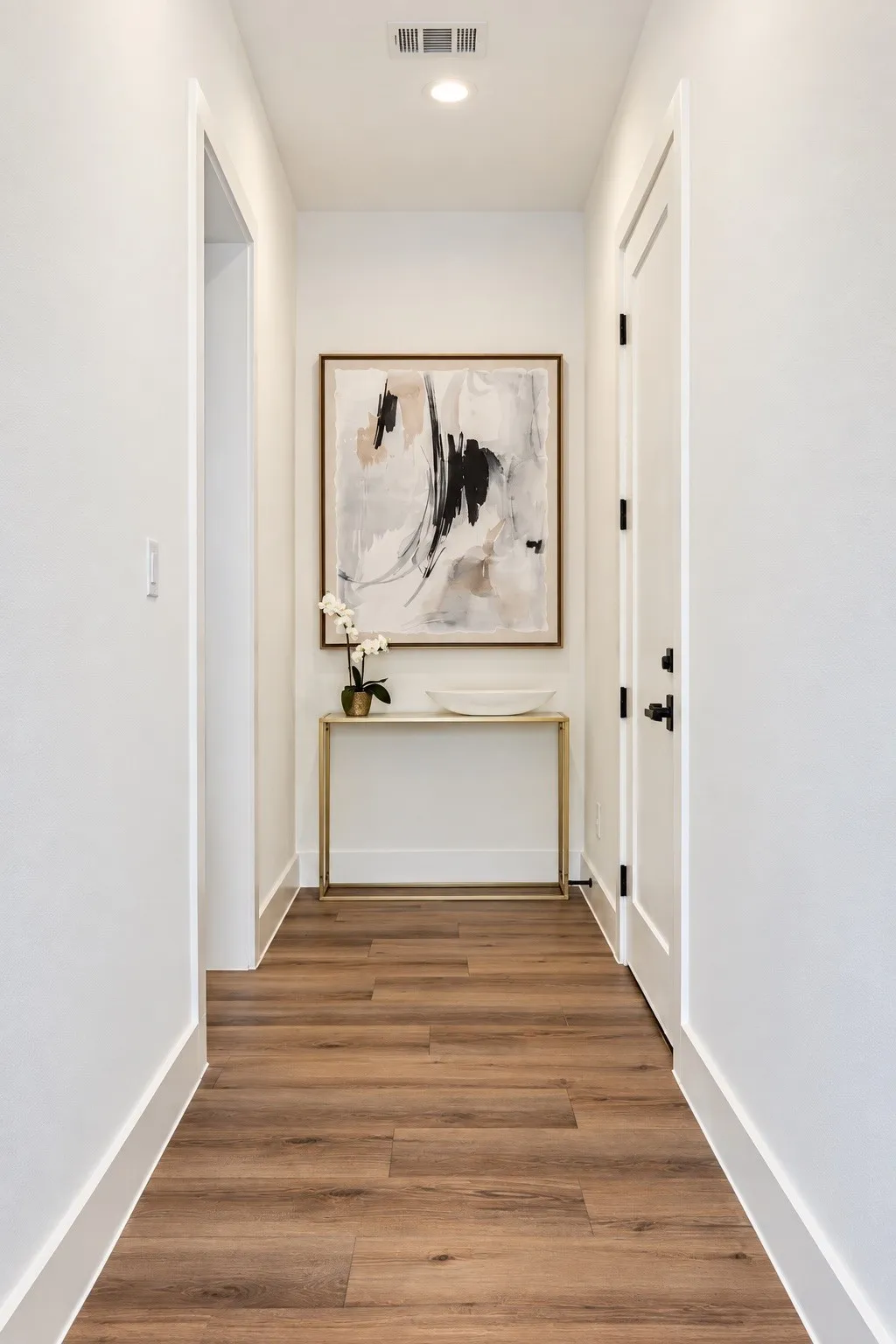 Recessed ceiling lighting, wood-finish flooring, white walls, white trim, and a white door with black hardware