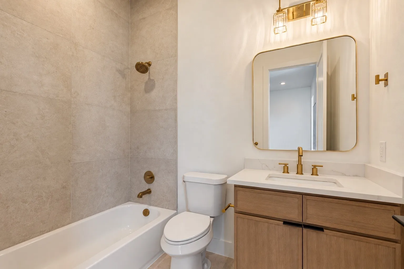 Bathtub with tile surround, toilet, vanity with integrated sink, gold-toned fixtures, and a framed mirror