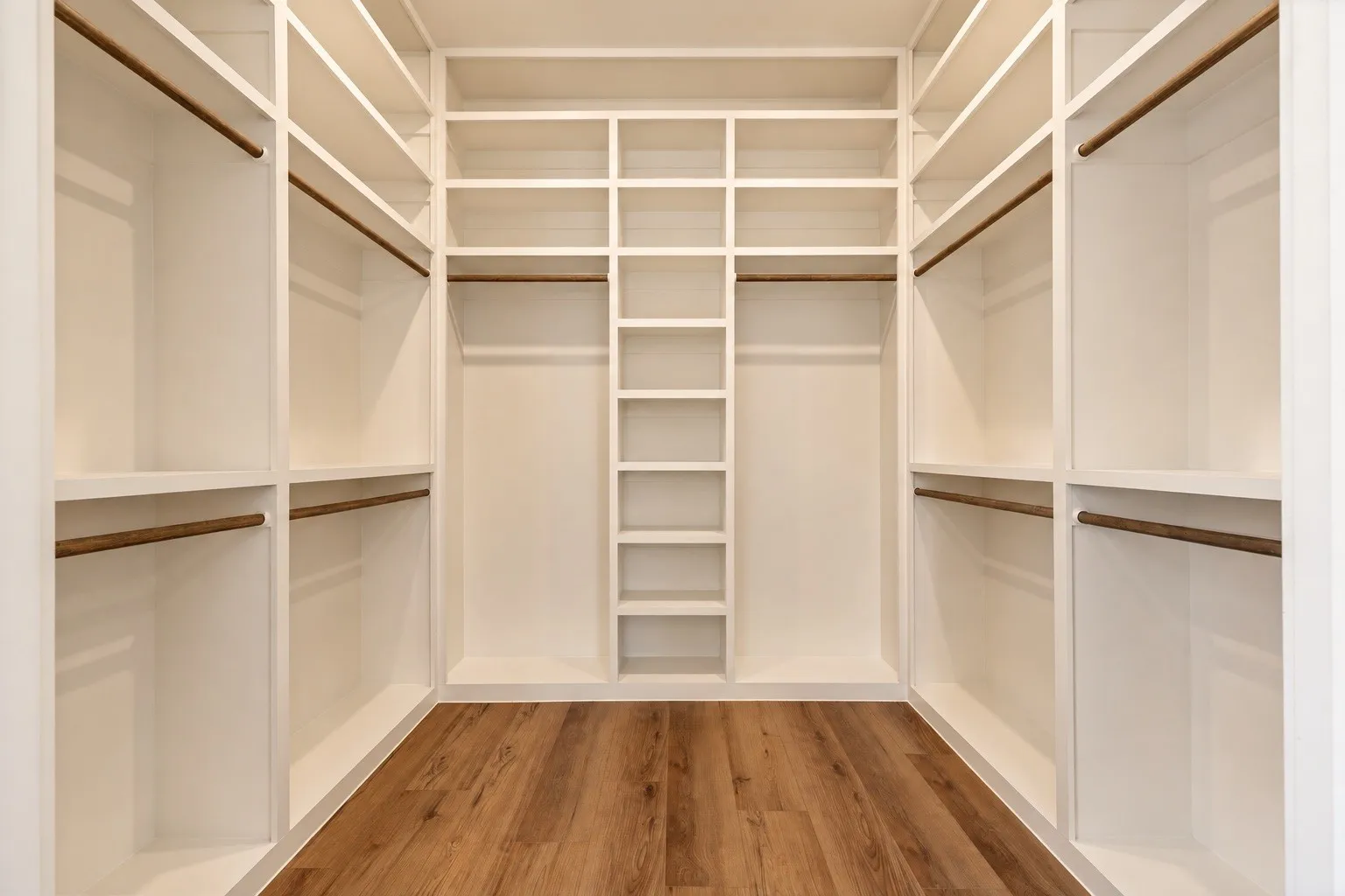 Built-in closet system with multiple shelving units, hanging rods, and wood-finish flooring