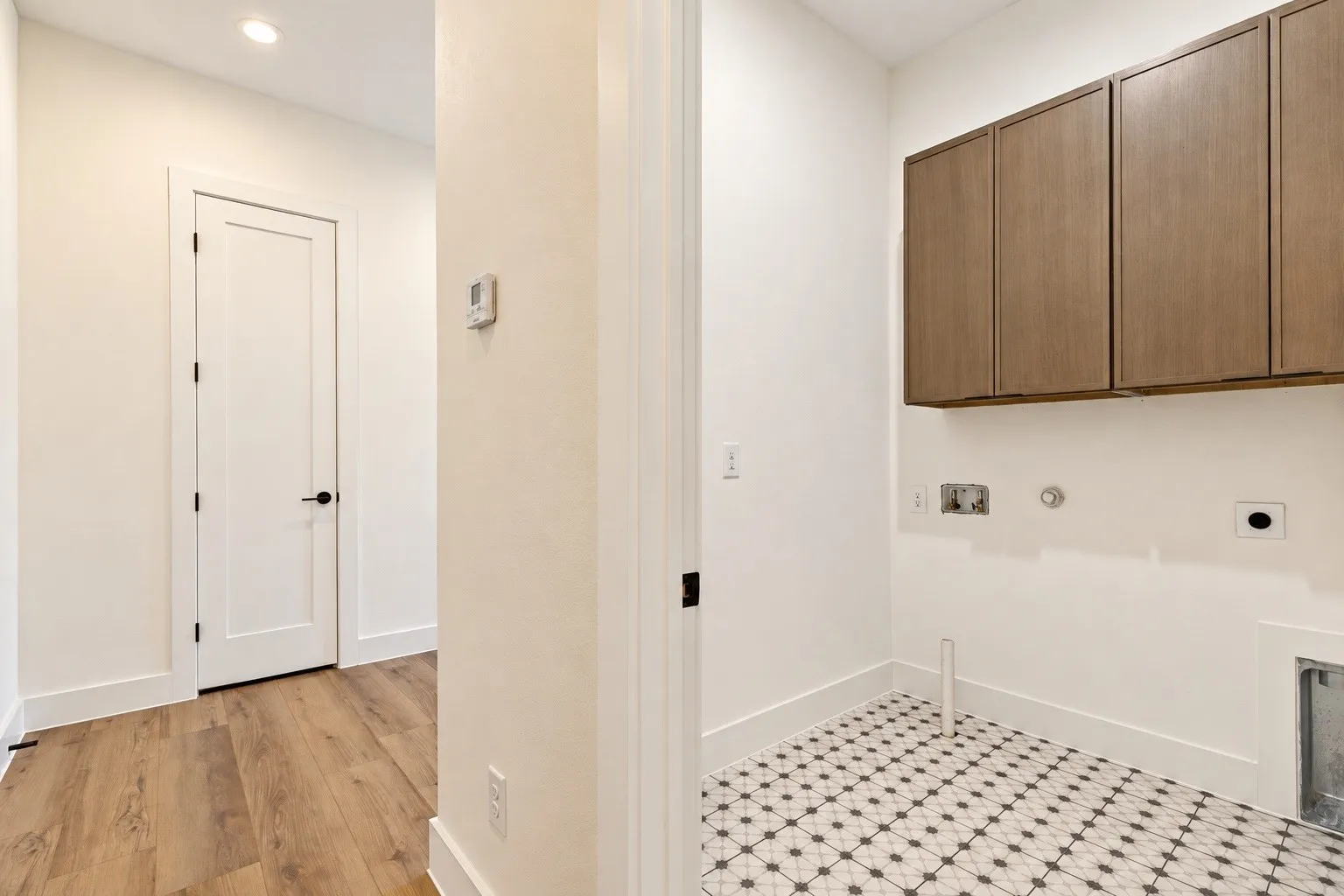 Utility space featuring patterned floor tile, wood-finish upper cabinetry, and a clean white color palette