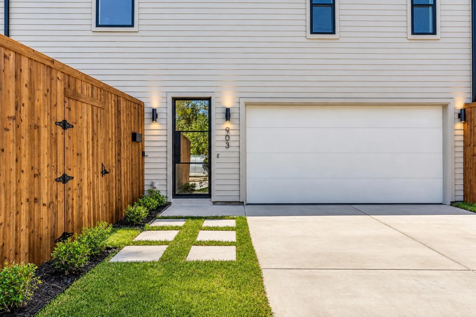 Horizontal siding, black-framed entry door, front yard landscaping, concrete driveway, and attached garage