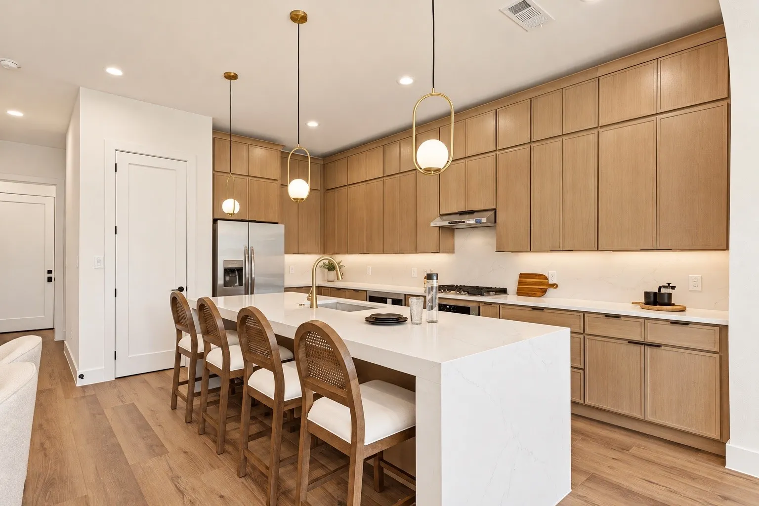 Kitchen featuring light wood-finish cabinetry, a large center island with a white countertop, stainless steel appliances, a gold-tone faucet, and wood-finish flooring