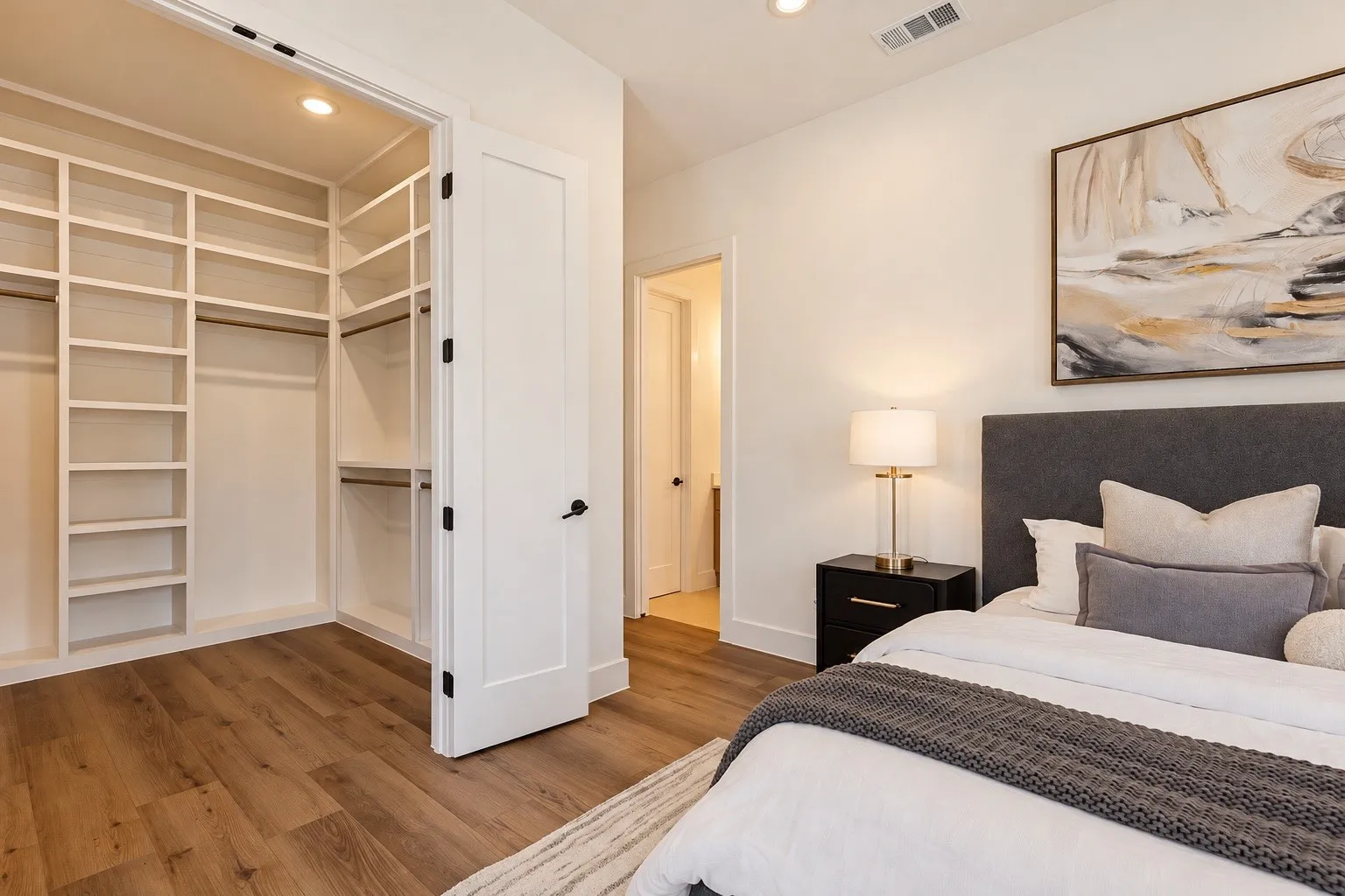Wood-finish flooring, built-in closet shelving, recessed lighting, and a solid core door with matte black hardware