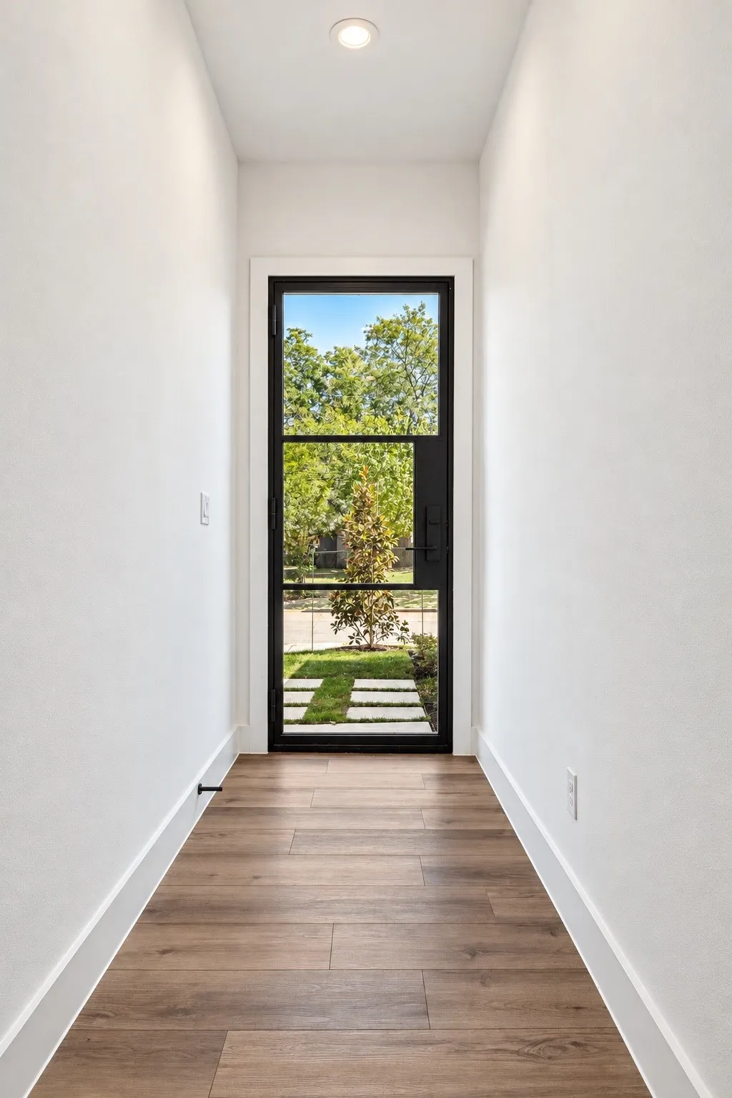 Black-framed glass entry door with wood-finish flooring and recessed ceiling lighting