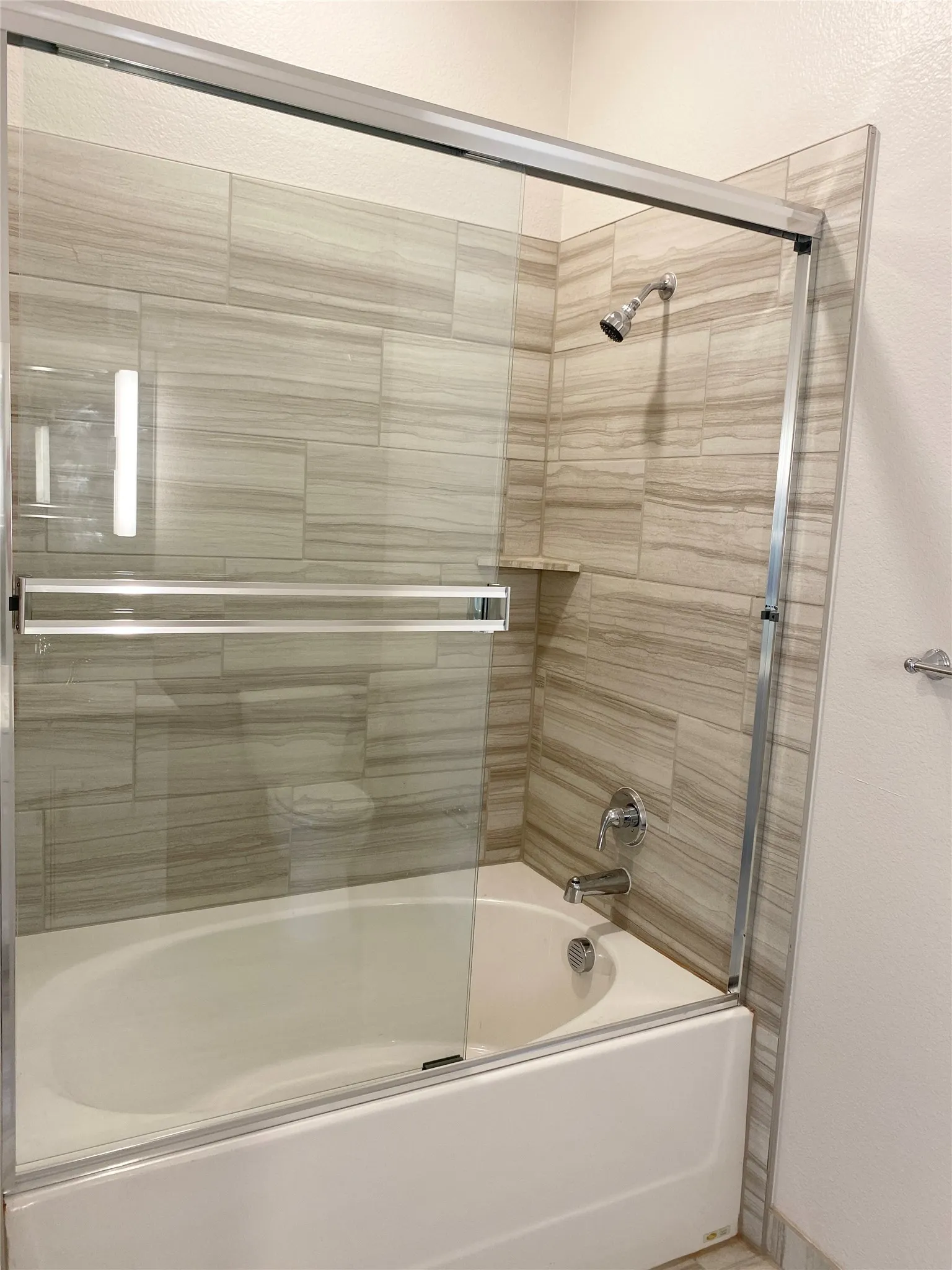 Bathtub with glass sliding shower doors, chrome fixtures, and a tiled surround with a built-in niche