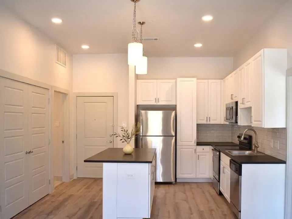 Modern kitchen featuring white shaker cabinetry, stainless steel appliances, black countertops, and a subway tile backsplash