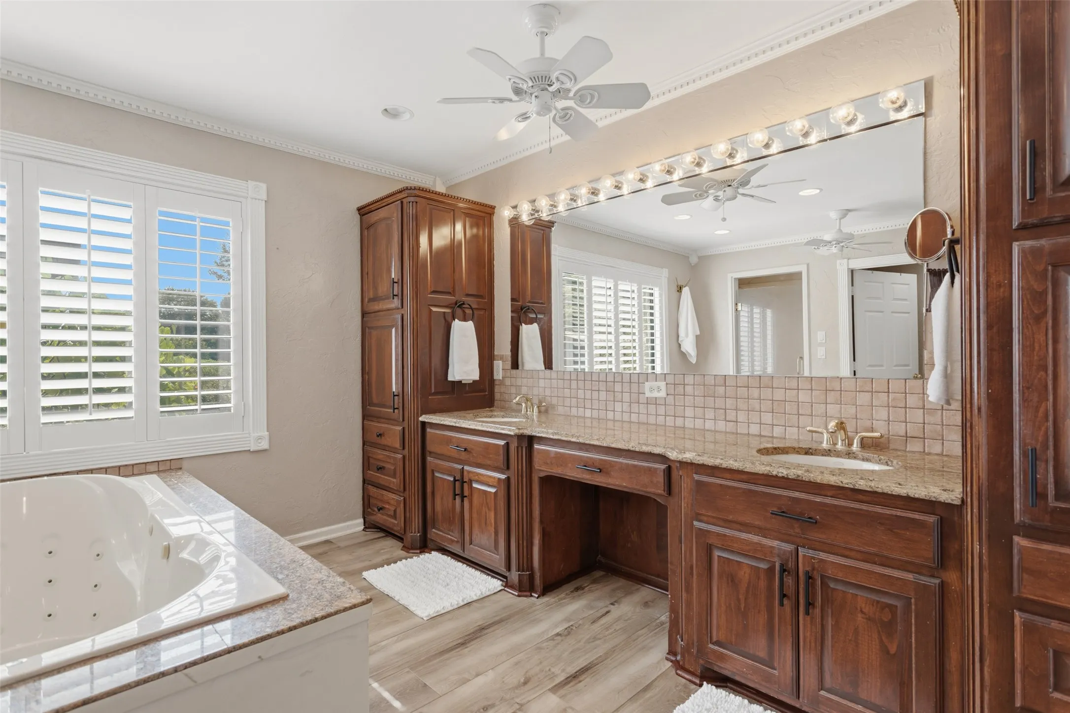 Built-in jetted tub, plantation shutters, wood-finish flooring, dual vanity with granite countertop, and extensive built-in cabinetry