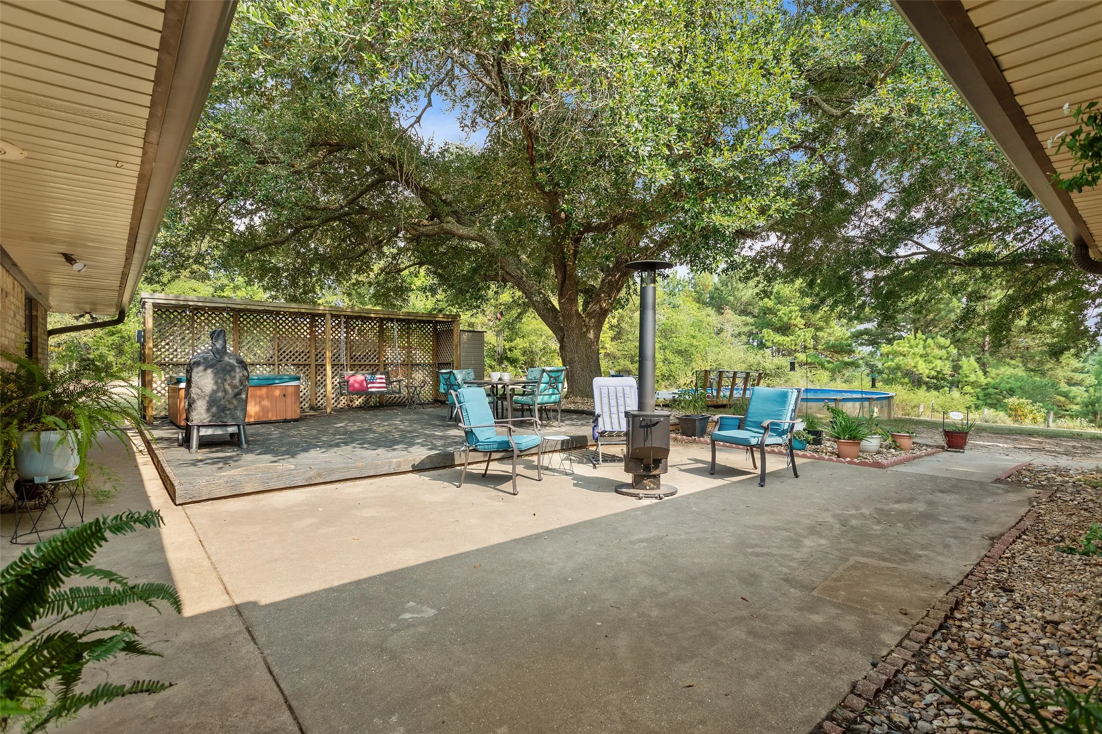 Expansive concrete patio with a covered section, mature tree, and surrounding natural landscaping