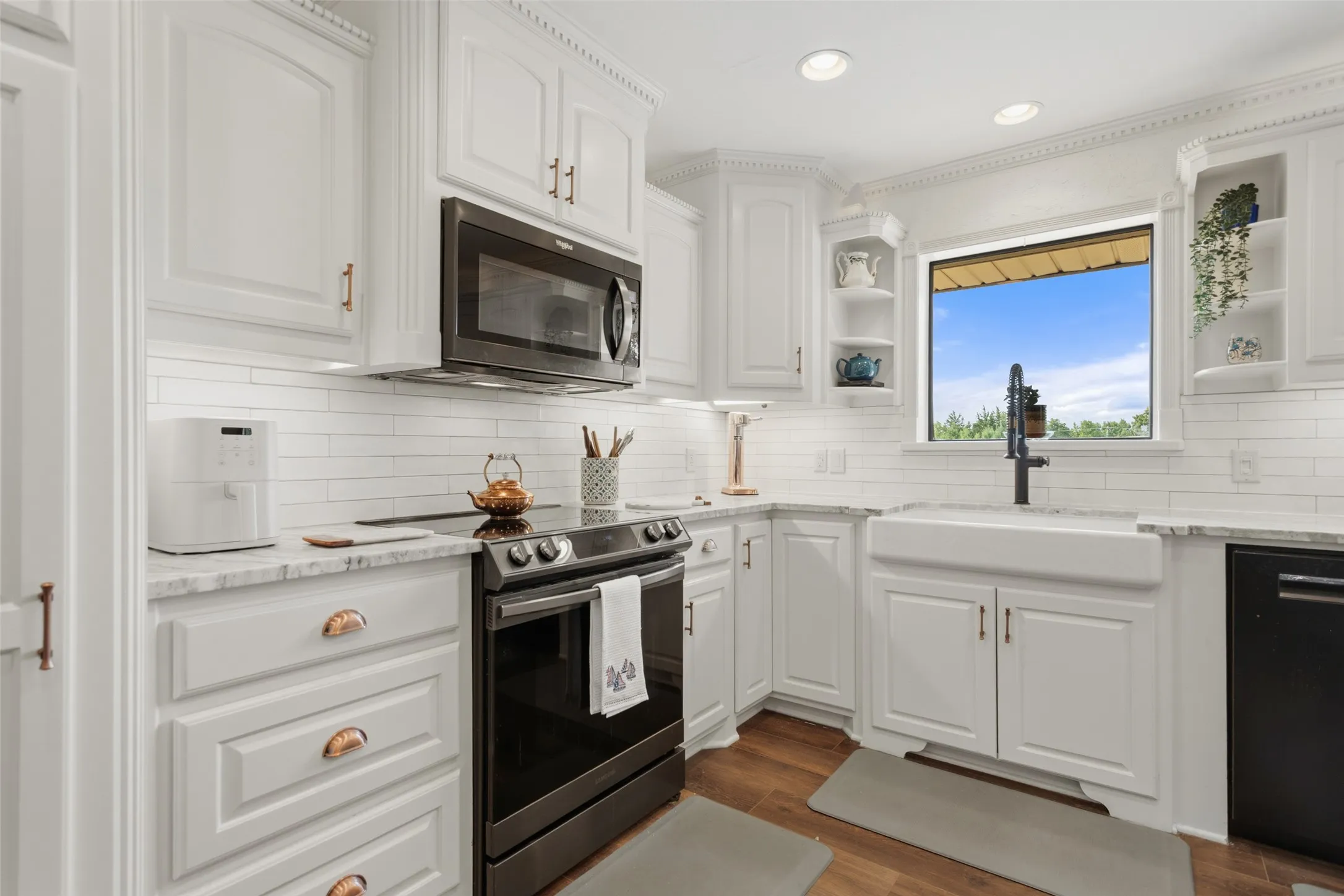 Bright, updated kitchen featuring white shaker cabinetry with brushed gold hardware, subway tile backsplash, stainless steel range with black finish, microwave, and white apron-front sink