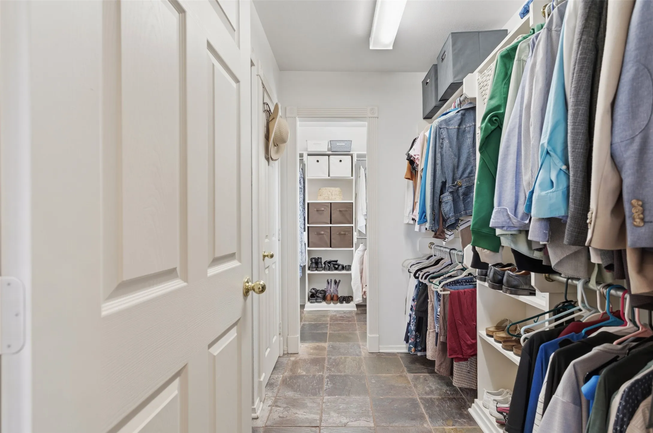 Walk-in closet featuring stone tile flooring, built-in shelving, and multiple hanging rods