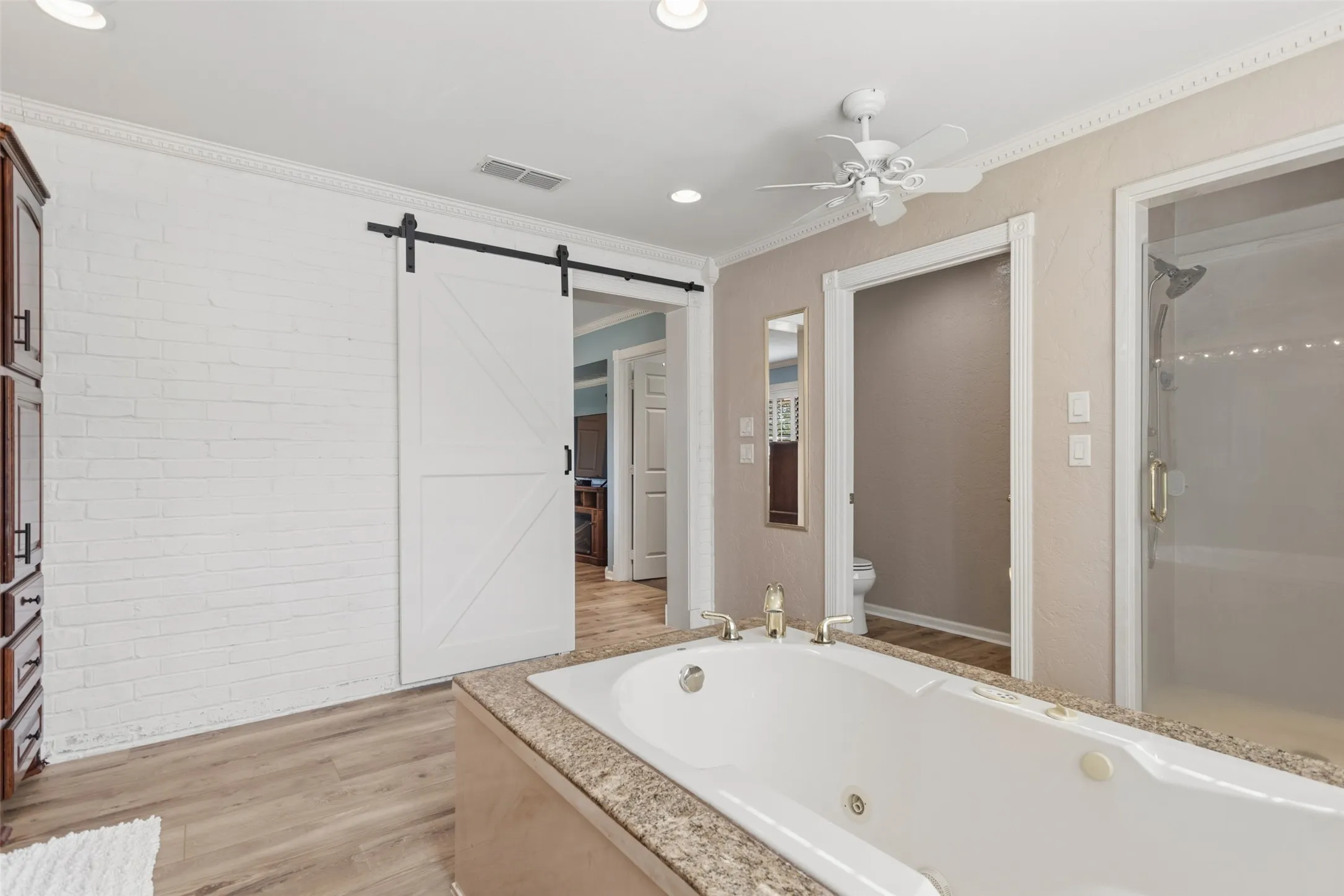 Soaking tub with a speckled countertop, walk-in shower with clear glass enclosure, ceiling fan, and wood-finish flooring