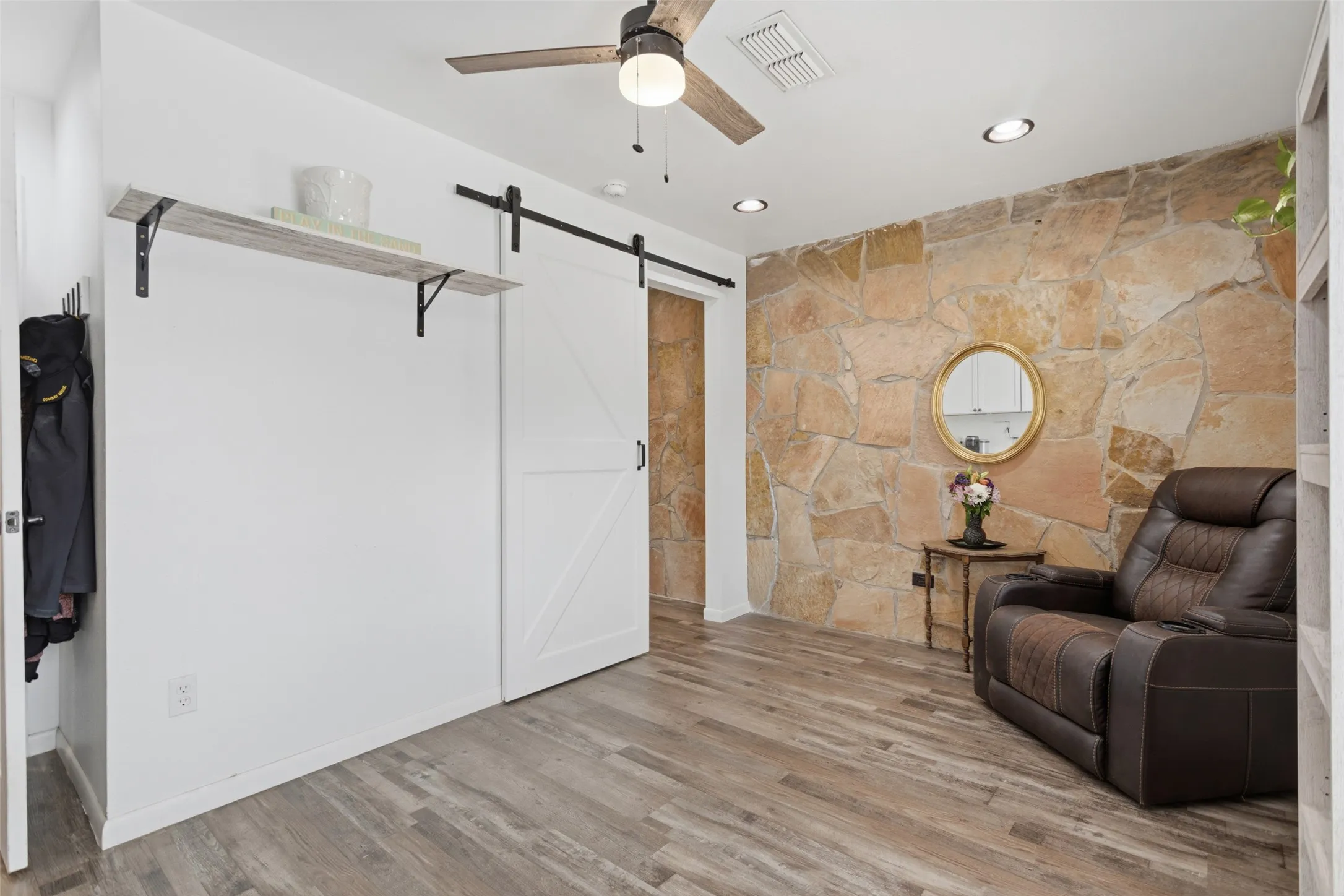 Wood-finish flooring, stone accent wall, recessed lighting, ceiling fan, and barn door