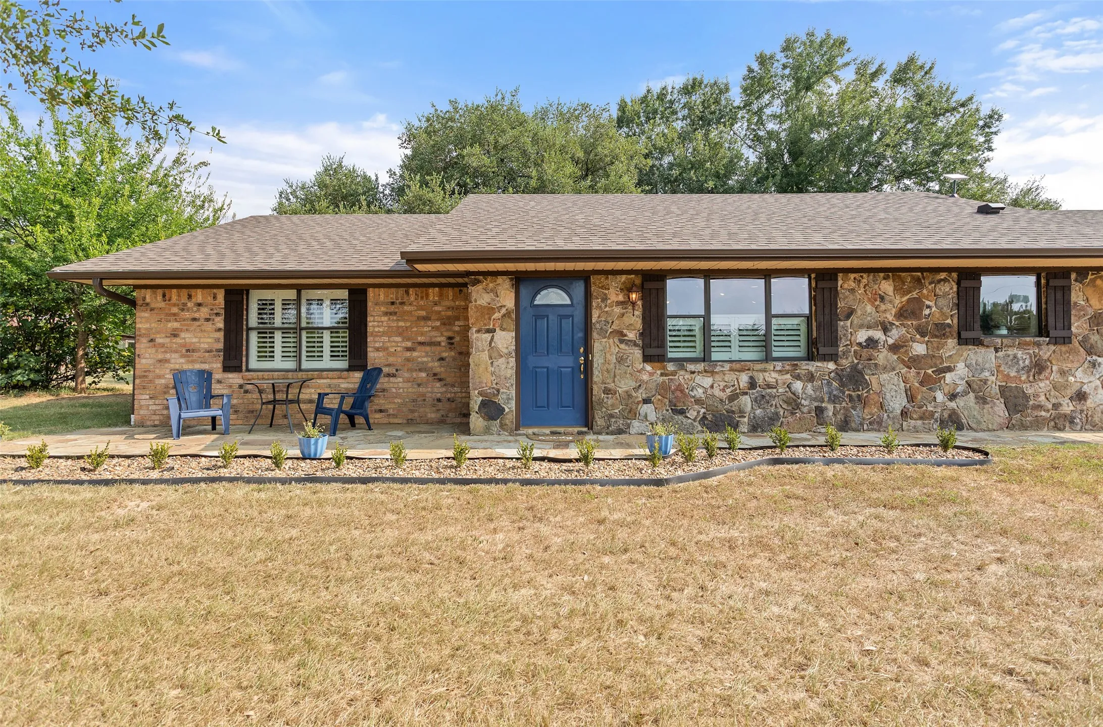 Stone and brick exterior with a prominent blue entry door, dark shutters, and a front patio