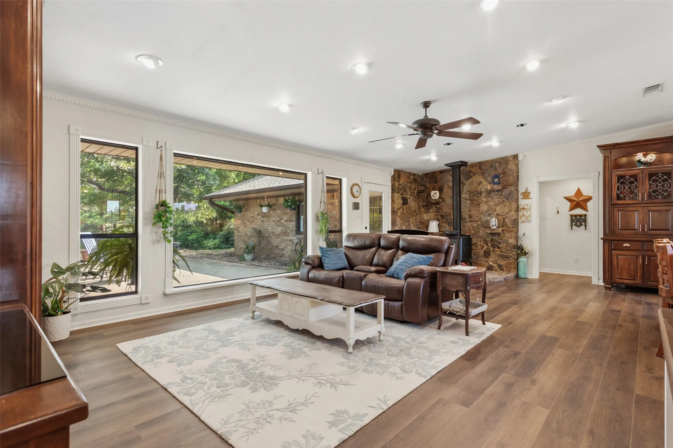 Spacious living area featuring extensive wood-finish flooring, a stone-clad wall with a wood-burning stove, recessed lighting, and a ceiling fan
