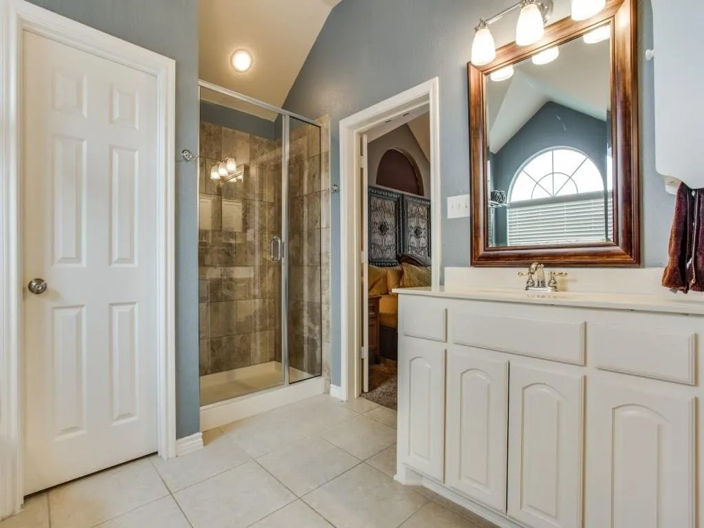 White single vanity with a laminate countertop, a framed mirror, a glass-enclosed shower, and tile​​‌​​​​‌​​‌‌​‌‌​​​‌‌​‌​‌​‌​​​‌​​ flooring