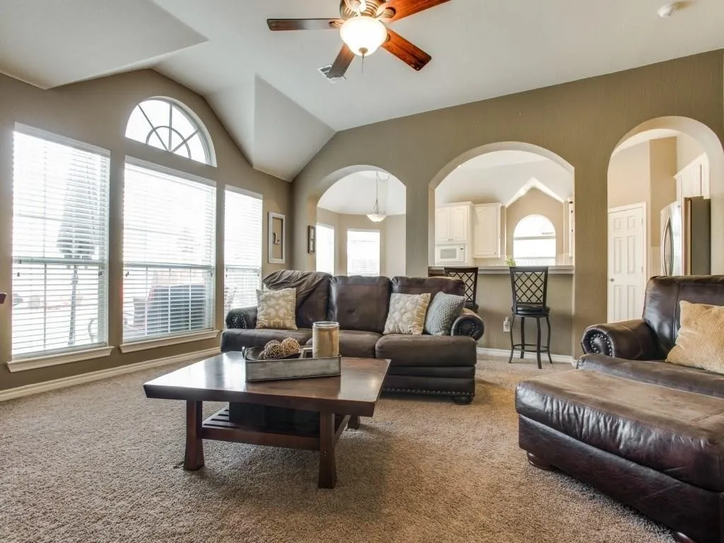 Vaulted ceiling with an attached ceiling fan, large arched windows, arched doorways, and light-colored carpeting