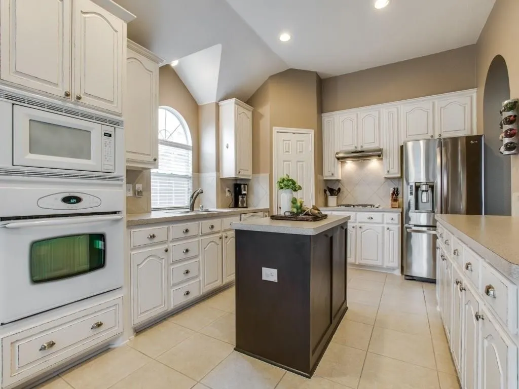 Kitchen featuring white cabinetry, a central island, stainless steel appliances, tile flooring, and vaulted ceilings