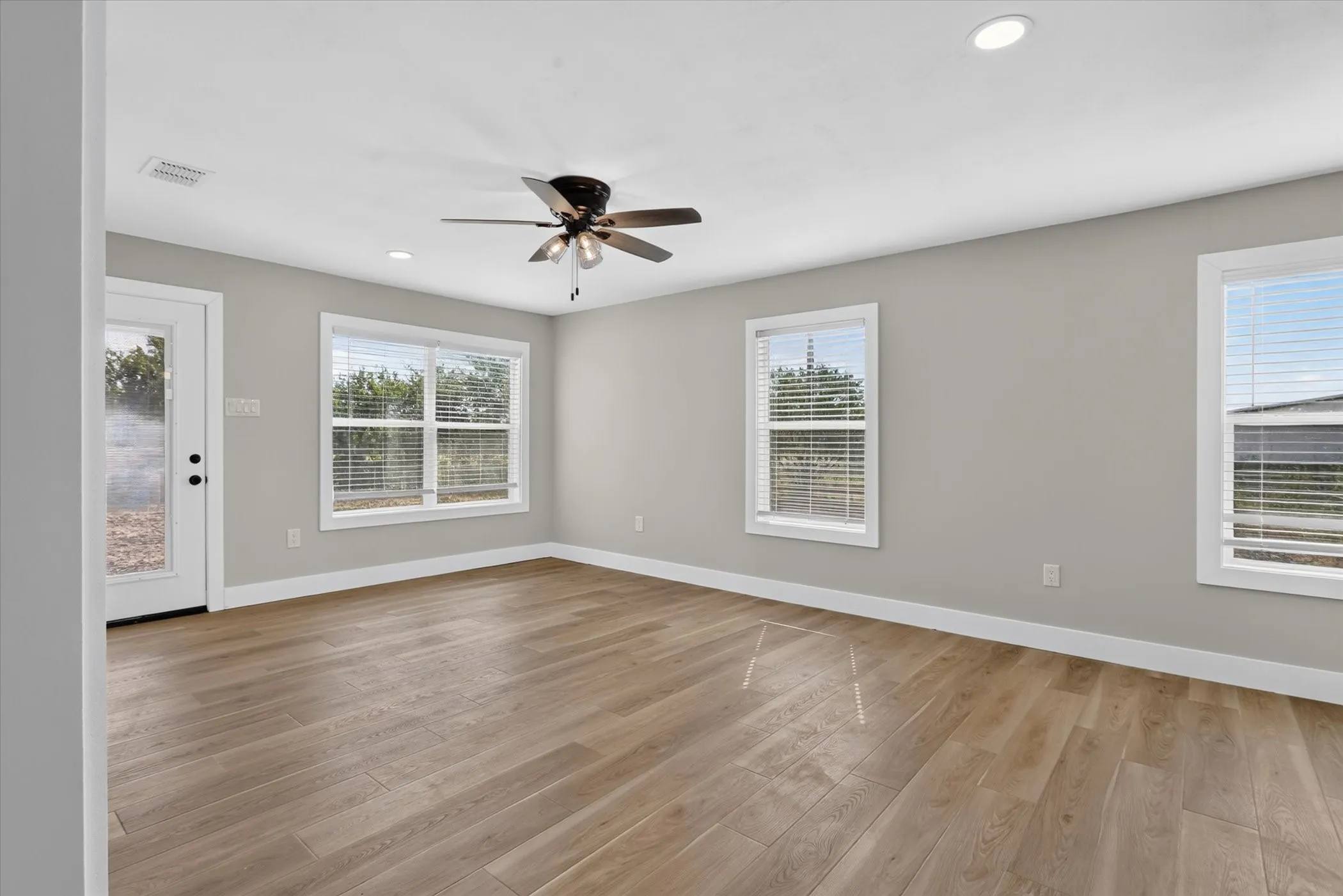 Wood-finish flooring, recessed lighting, ceiling fan, multiple windows, and a white glass-paneled door