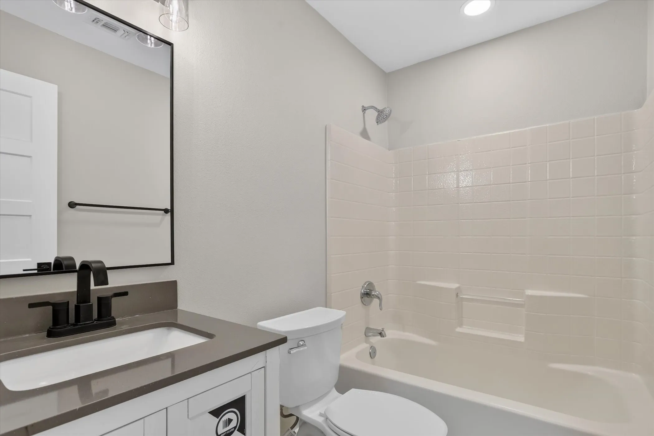 Bathroom featuring a vanity with an integrated sink and countertop, matte black faucet, framed mirror, and a shower-tub combination with tiled walls