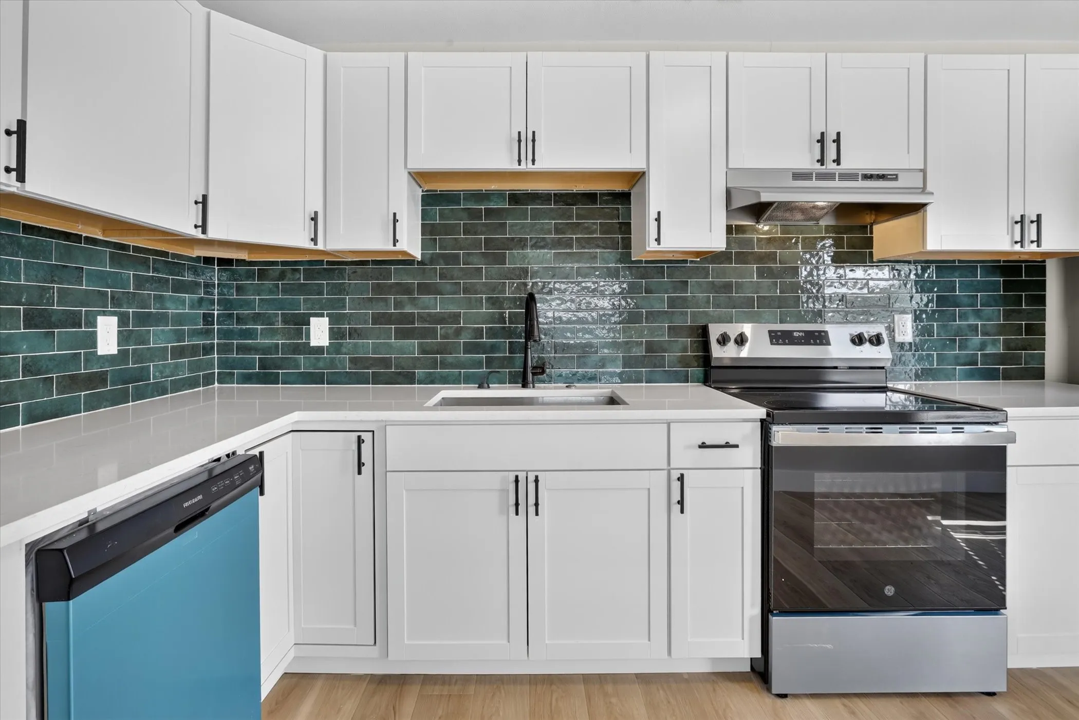 White shaker-style cabinetry with matte black hardware, a dark teal subway tile backsplash, and light-toned countertops