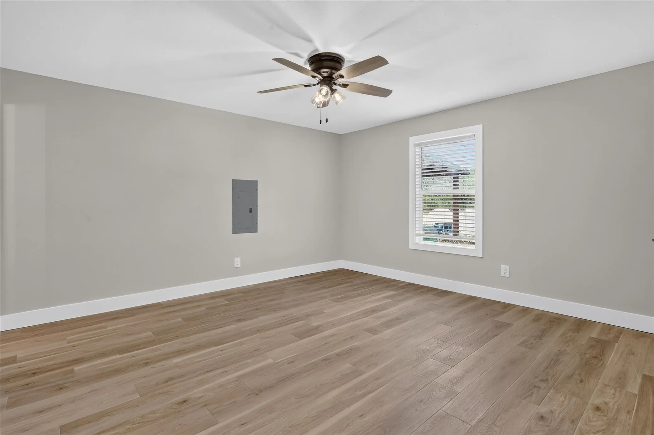 Wood-finish flooring, neutral wall tones, white trim, window with blinds, and a ceiling fan with integrated lighting