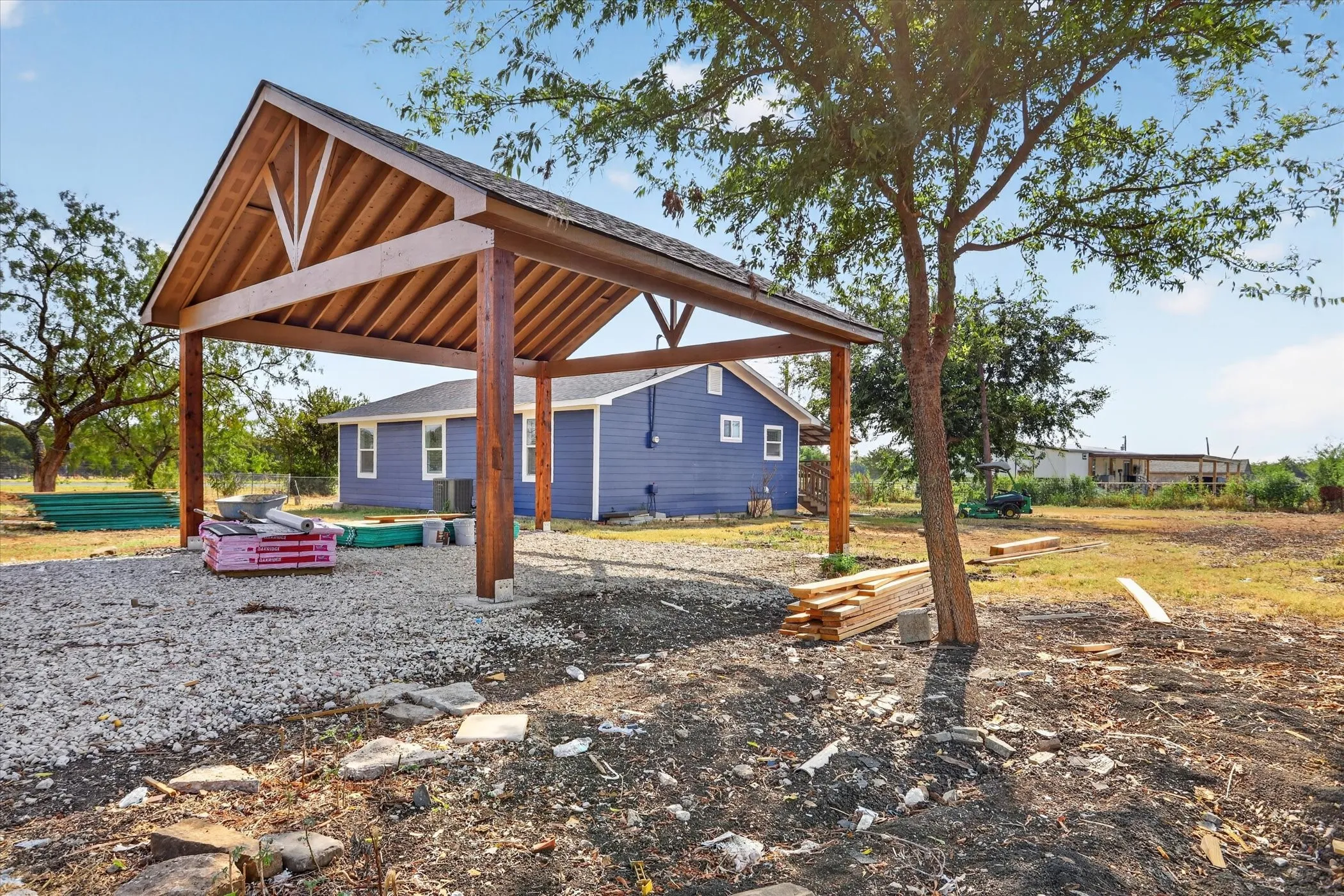 Open-air carport with exposed wood beams and posts, situated on a gravel surface
