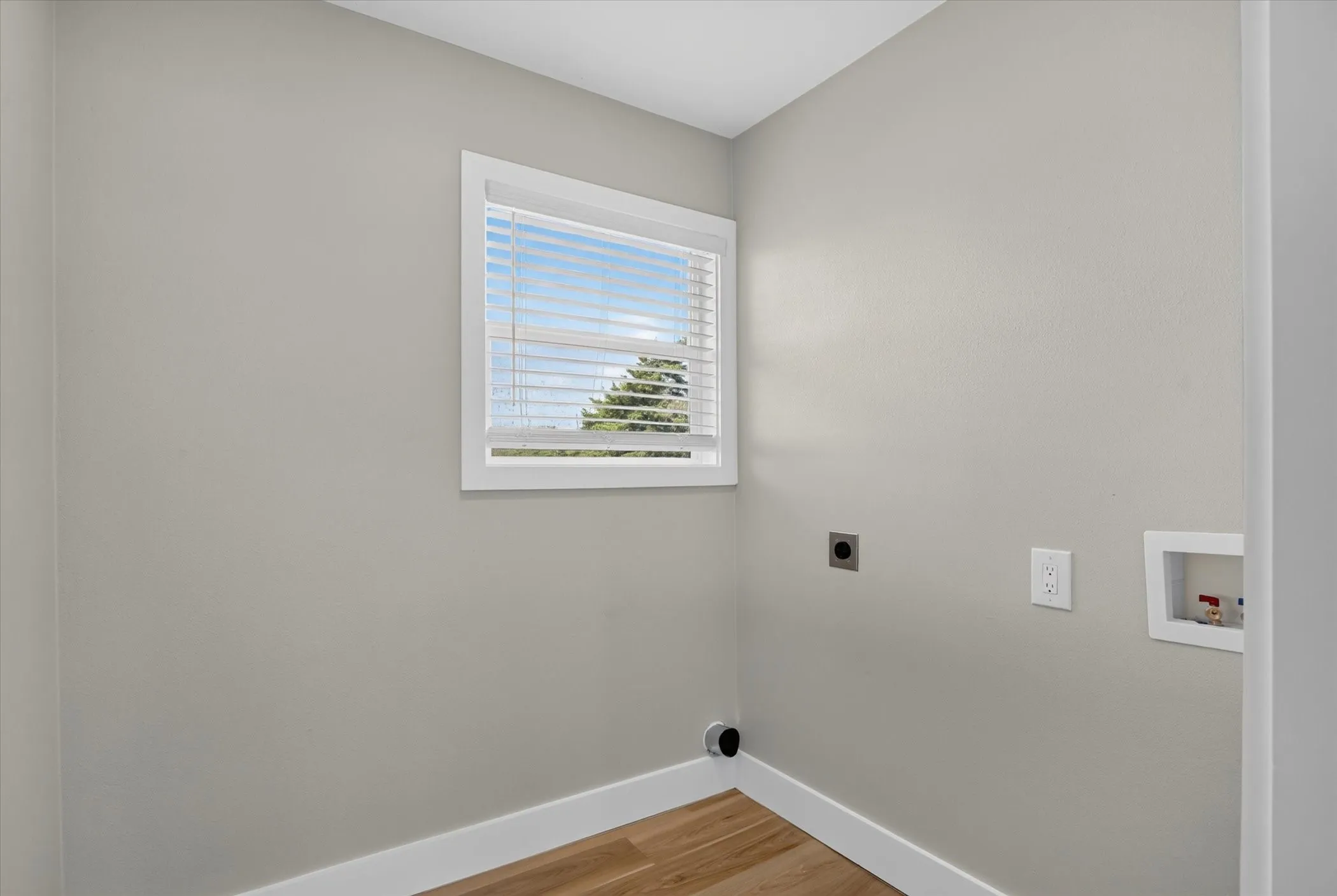 Light-toned painted walls with a white framed window, wood-finish flooring, and white trim