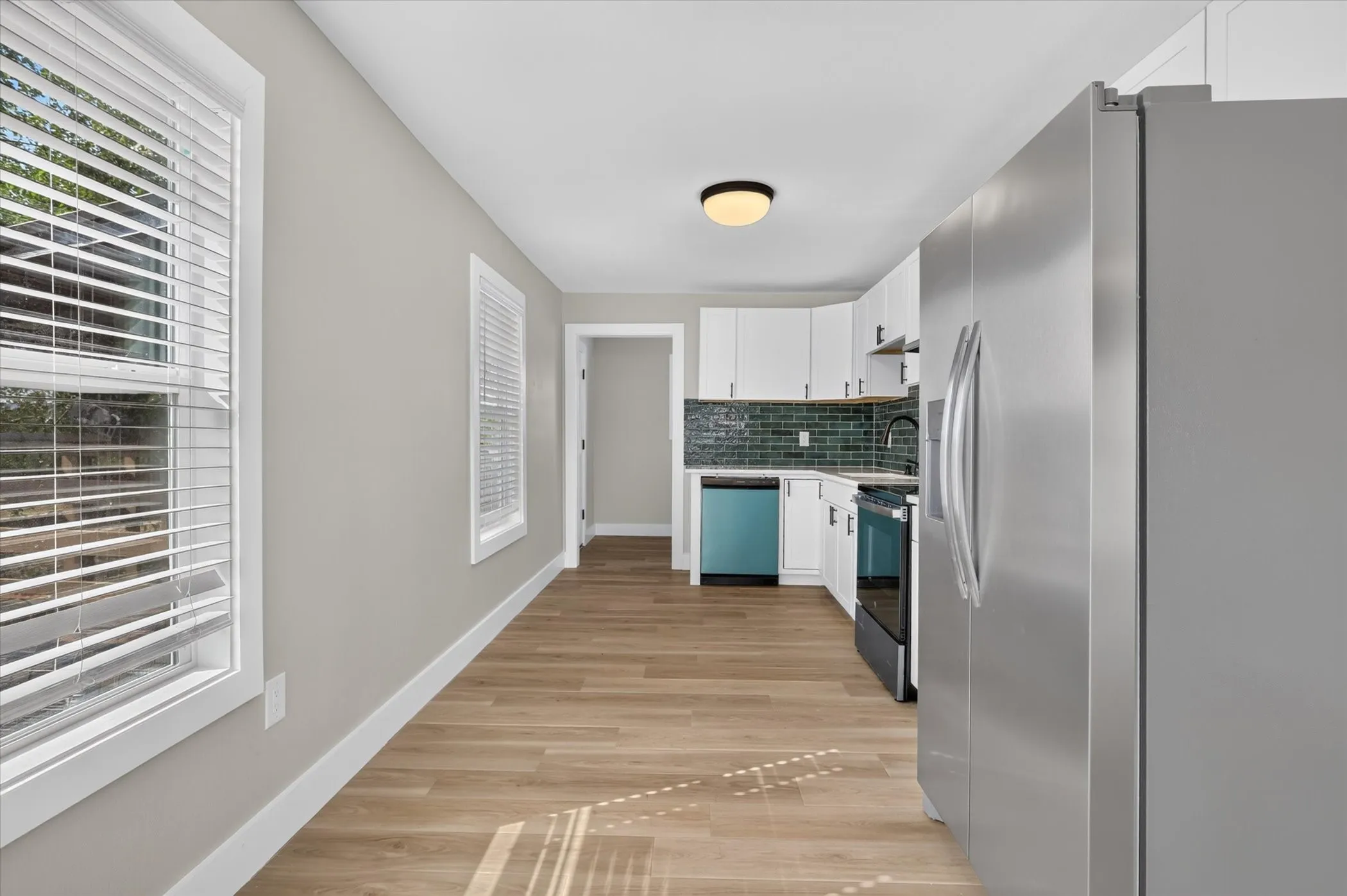 Stainless steel refrigerator and range, integrated dishwasher, subway tile backsplash, white cabinetry, and wood-finish flooring