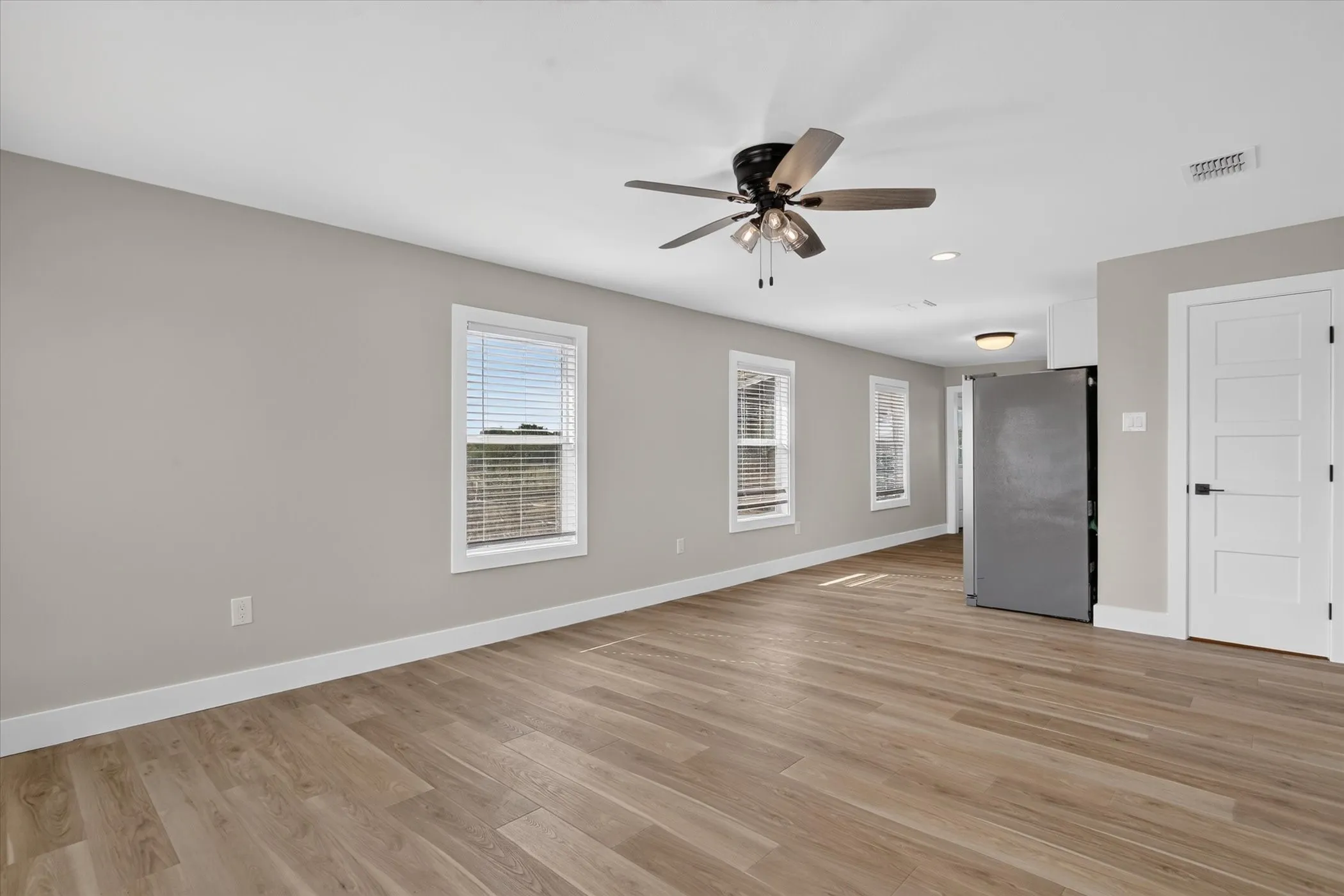 Expansive interior with wood-finish flooring, light gray walls, multiple windows, and a ceiling fan